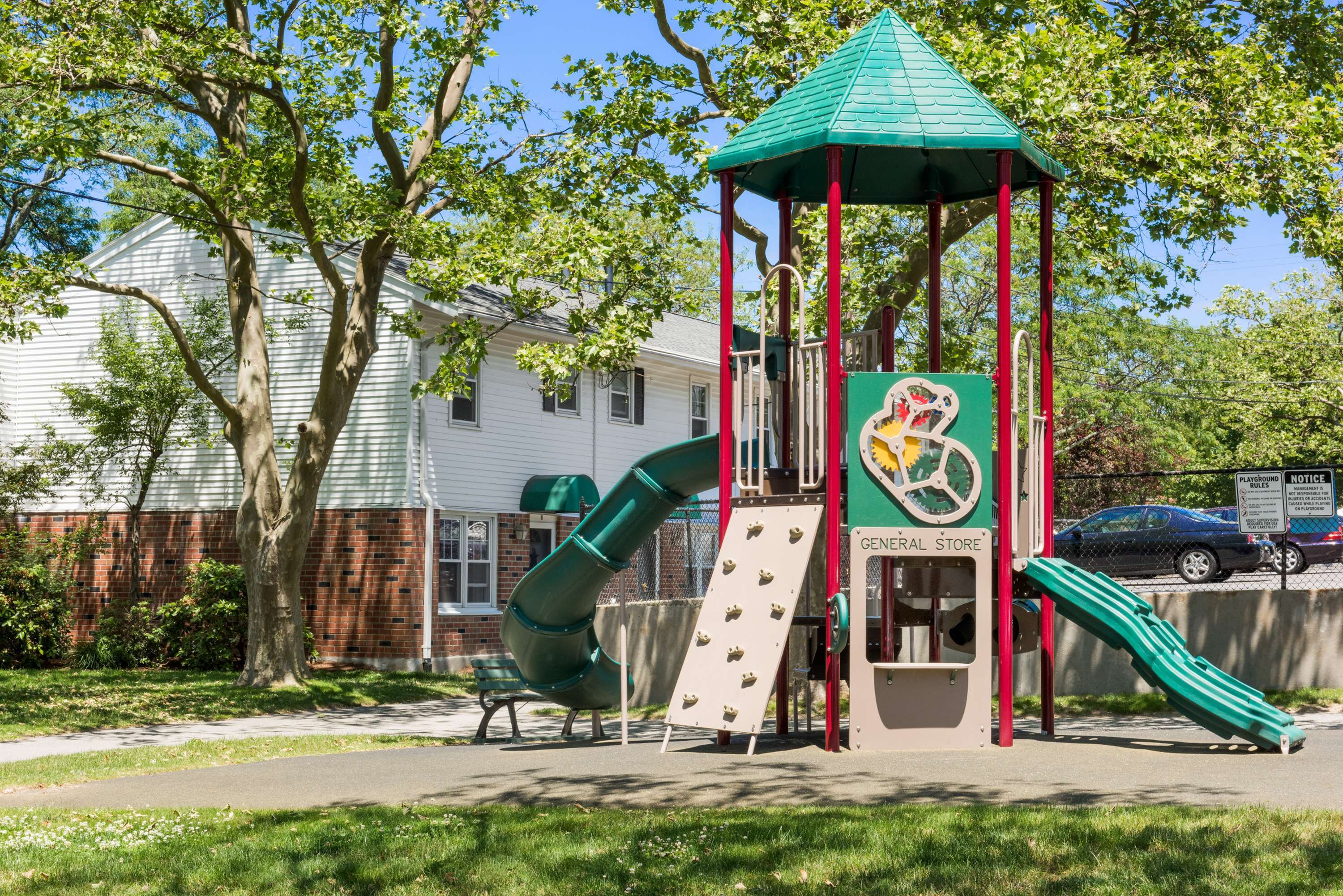 Charming apartment community playground with colorful slides and climbing structures surrounded by lush trees and vibrant greenery.