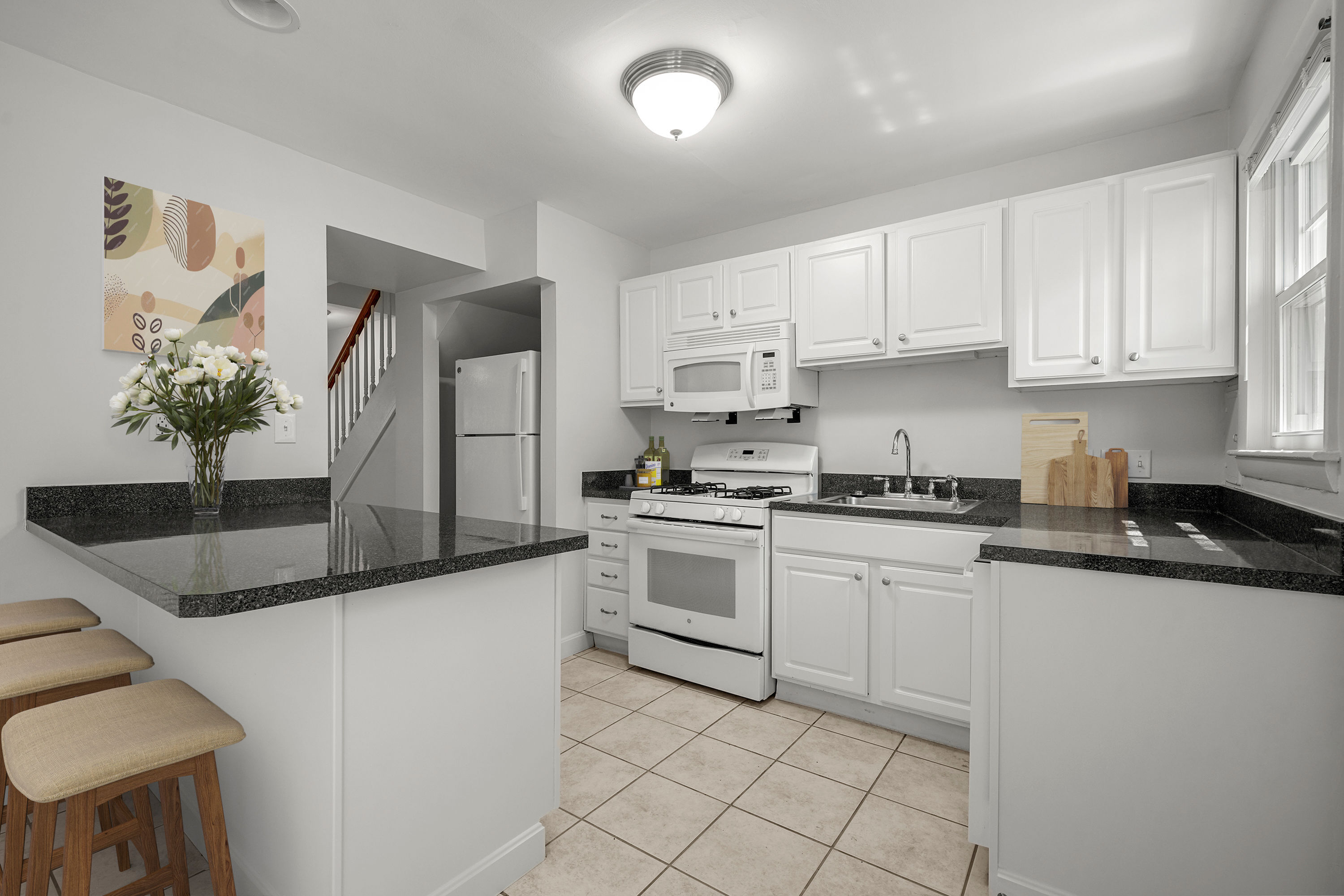 Modern kitchen with sleek black countertops, white cabinetry, and a cozy breakfast bar featuring upholstered stools.