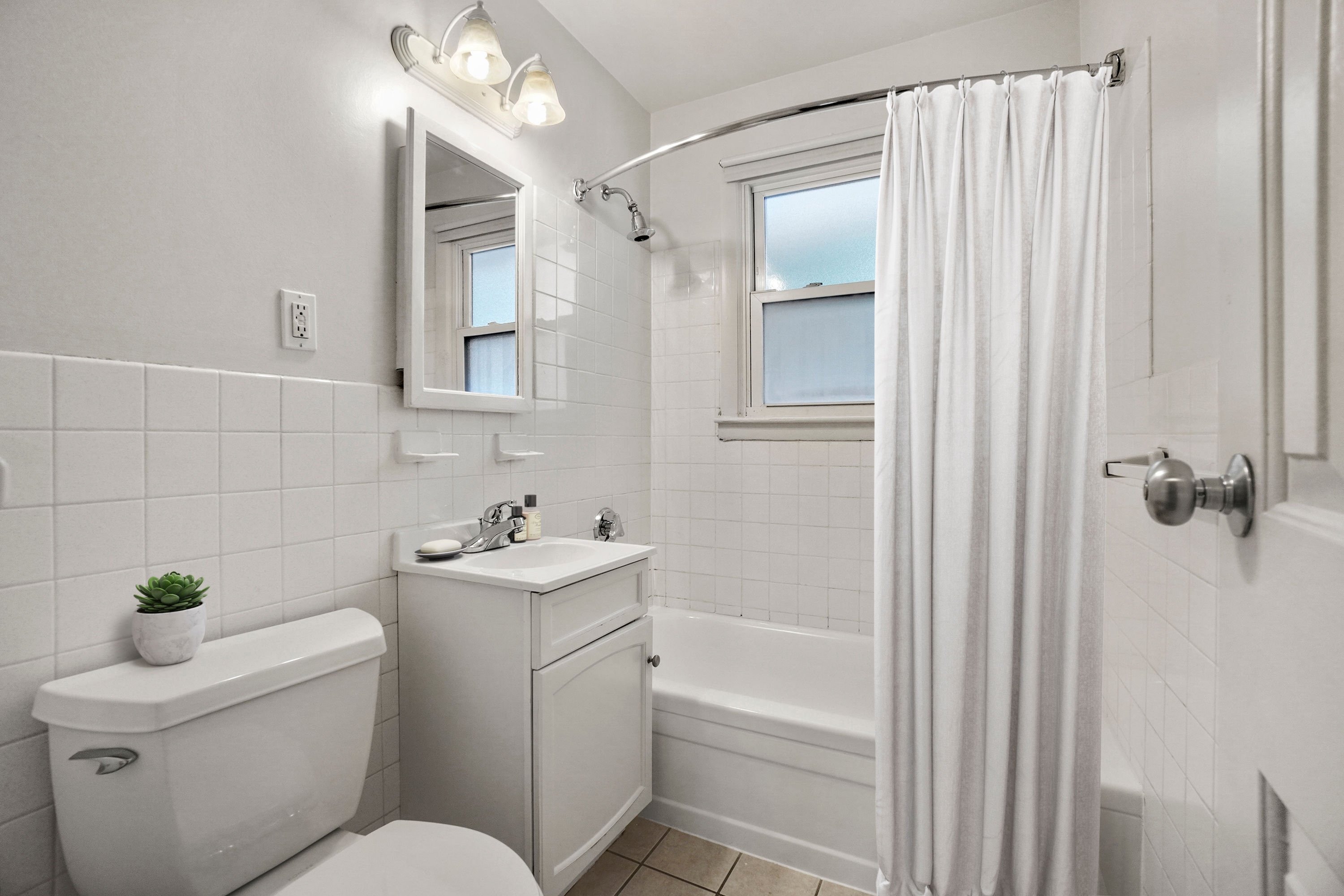 Bright and modern bathroom with elegant white tiles, sleek fixtures, and a cozy bathtub perfect for relaxation.
