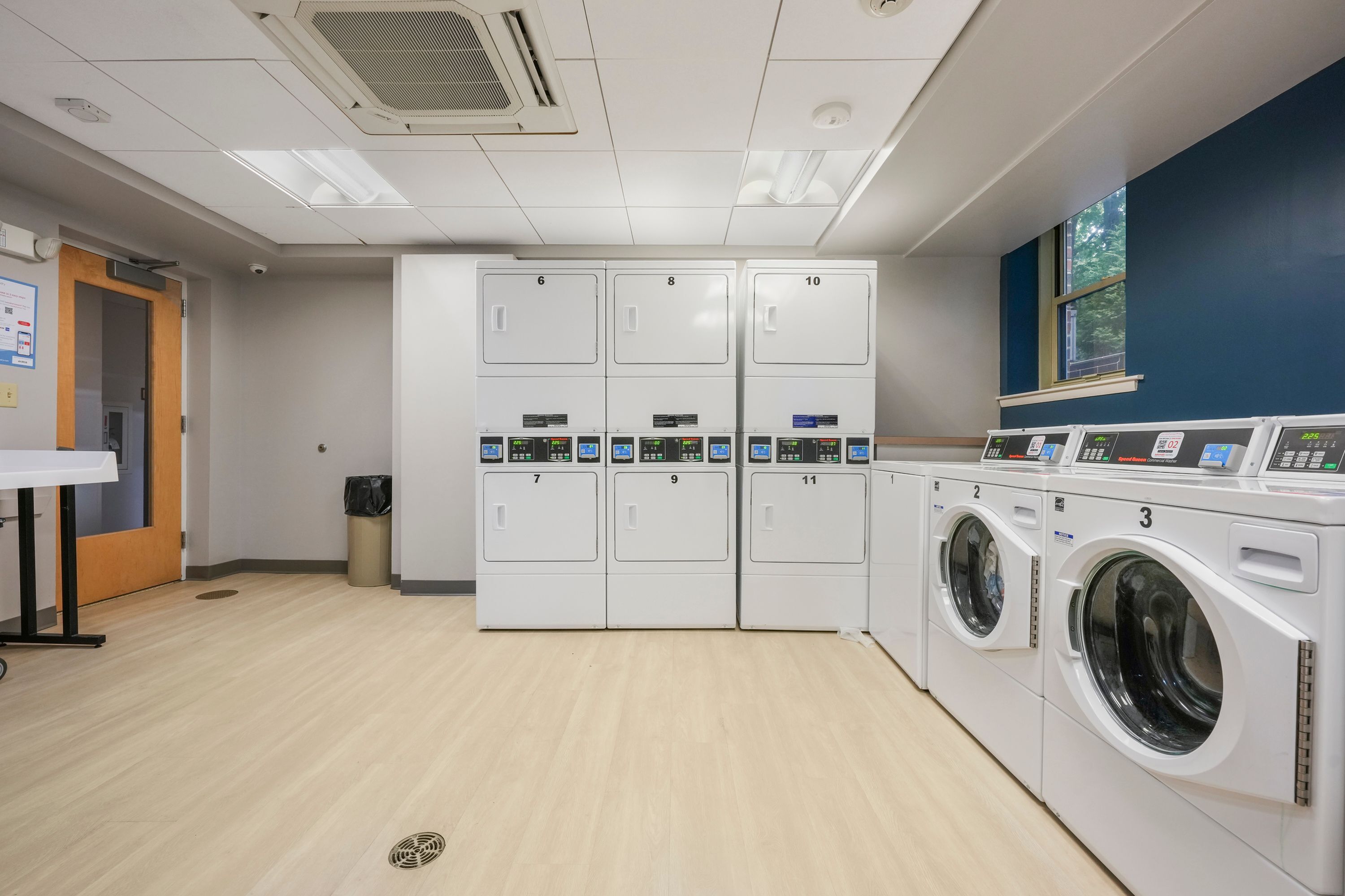 Modern apartment laundry room with multiple high-efficiency washers and dryers, ample space, and bright lighting.