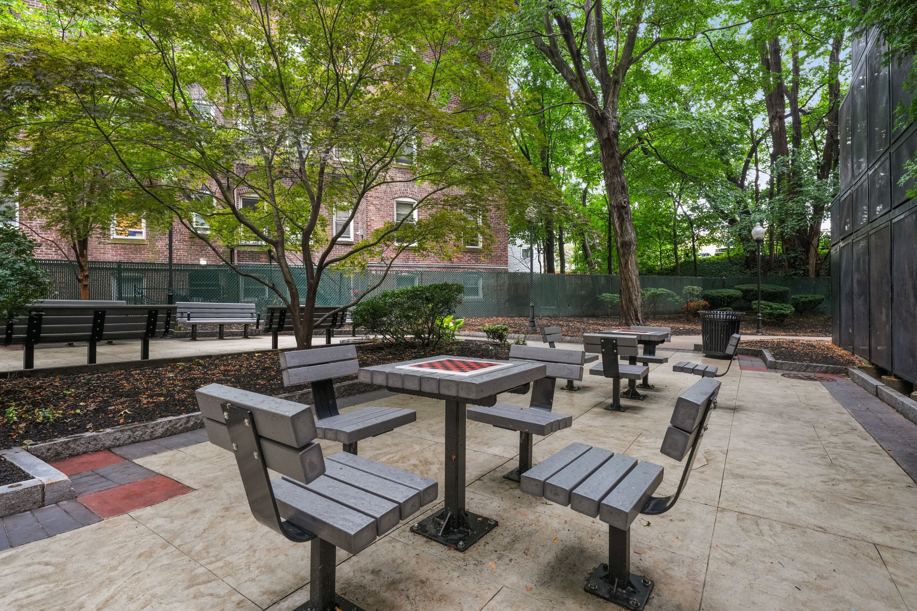 Charming outdoor courtyard with modern picnic tables surrounded by lush greenery, perfect for relaxing and socializing in a serene urban setting.