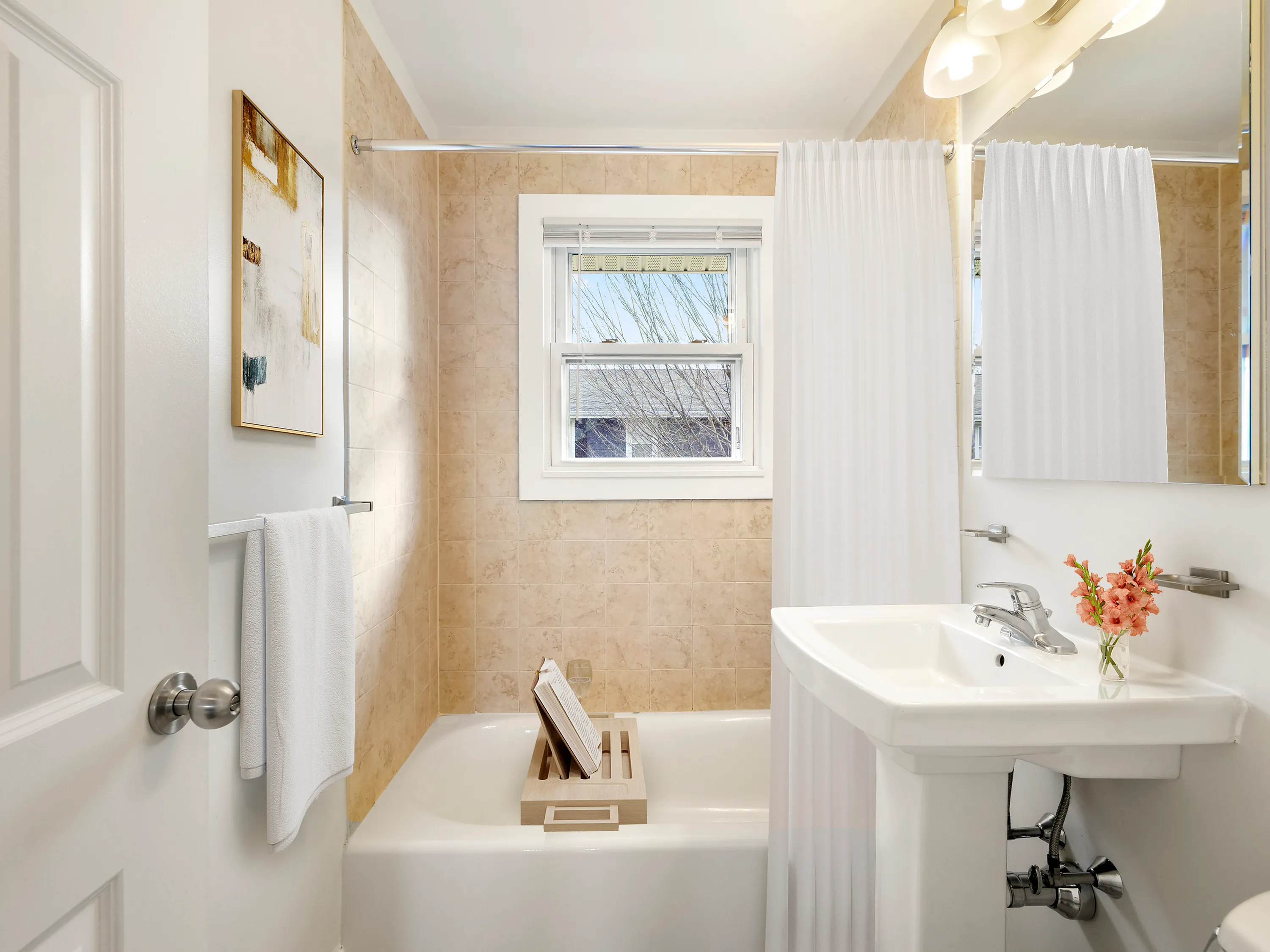 Bright and elegant bathroom with modern fixtures, featuring a cozy bathtub, chic vanity, and a serene window view.