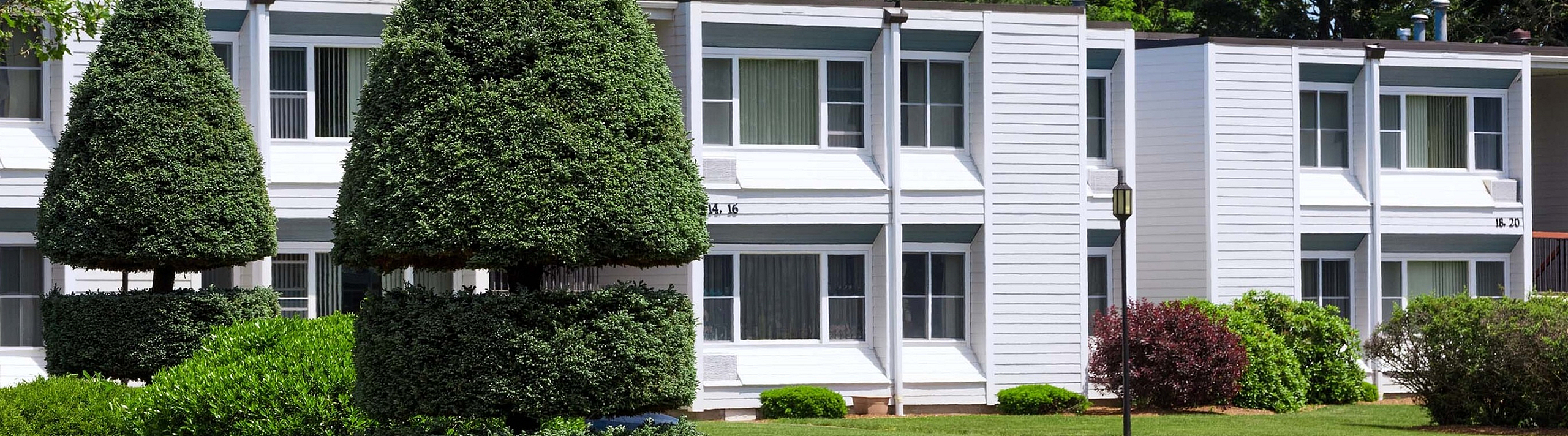 Charming residential complex with well-maintained landscaping, featuring modern white two-story buildings surrounded by lush greenery and artfully shaped trees.