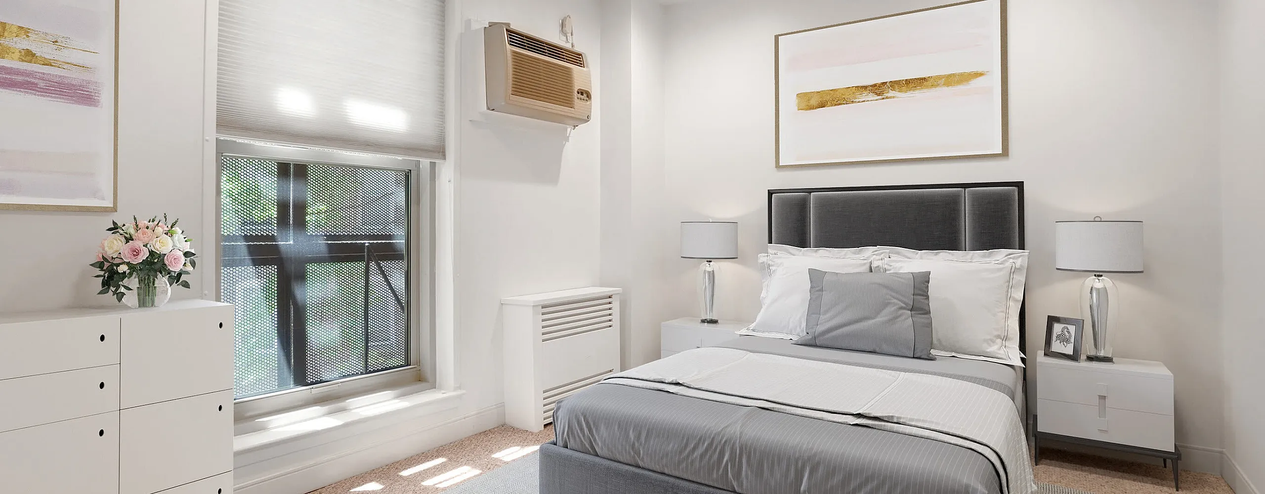 Bright and elegant bedroom with a modern gray bed, chic artwork, and soft carpeting enhanced by natural light.