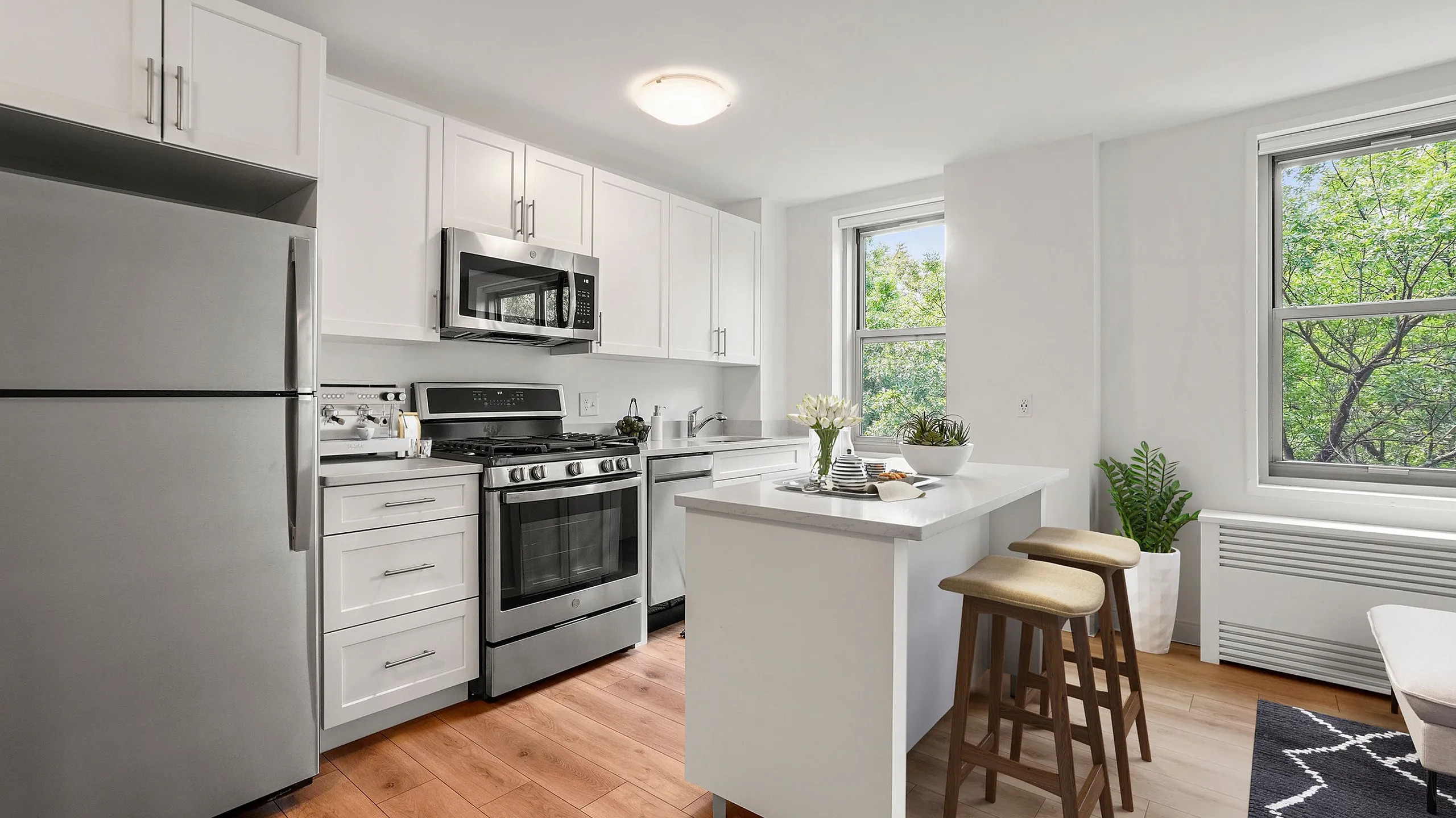 Chic modern kitchen with stainless steel appliances, white cabinetry, and an inviting breakfast bar next to large sunlit windows.