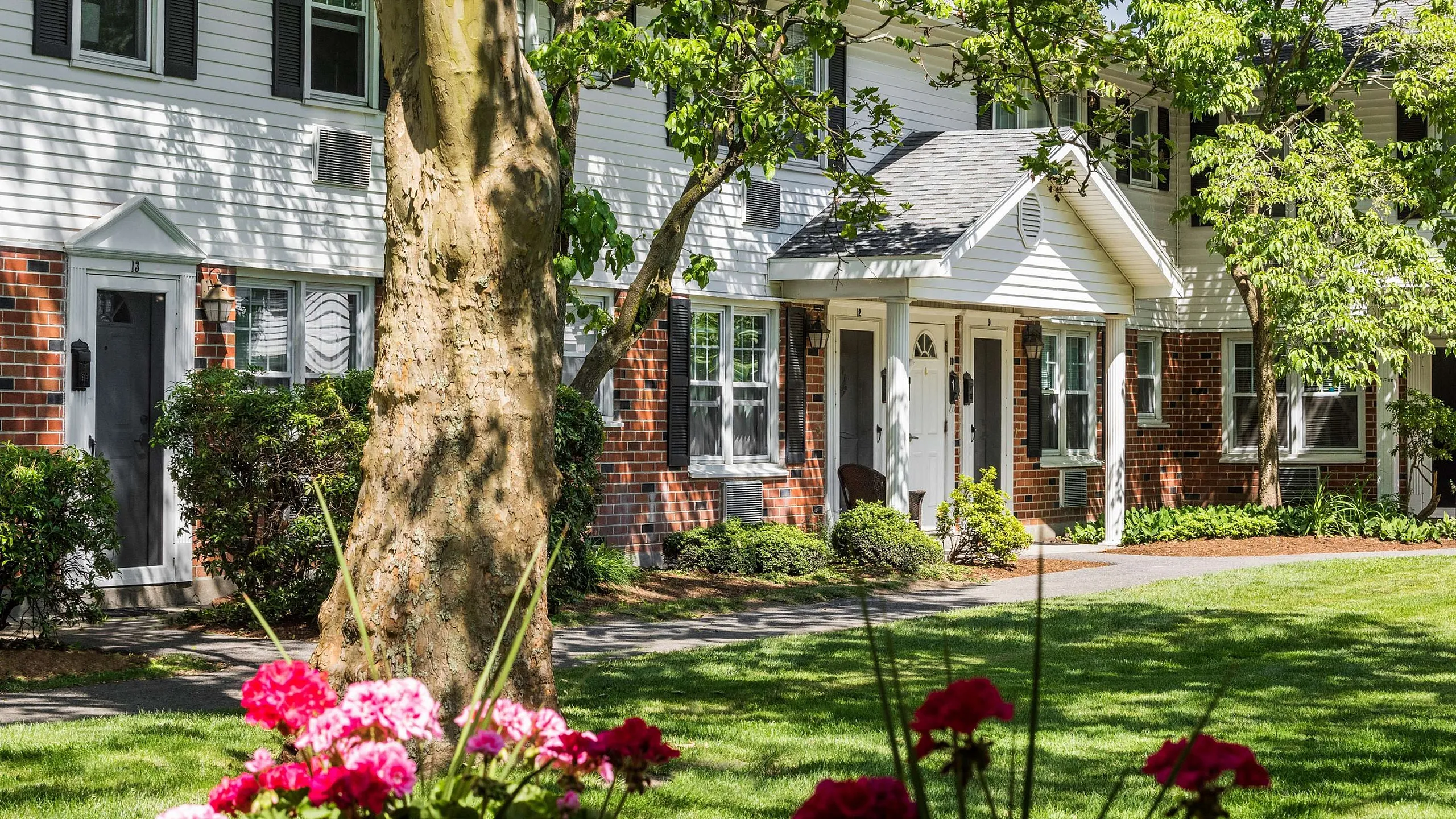 Charming townhouse with classic brick facade and lush green lawn accented by vibrant pink flowers.