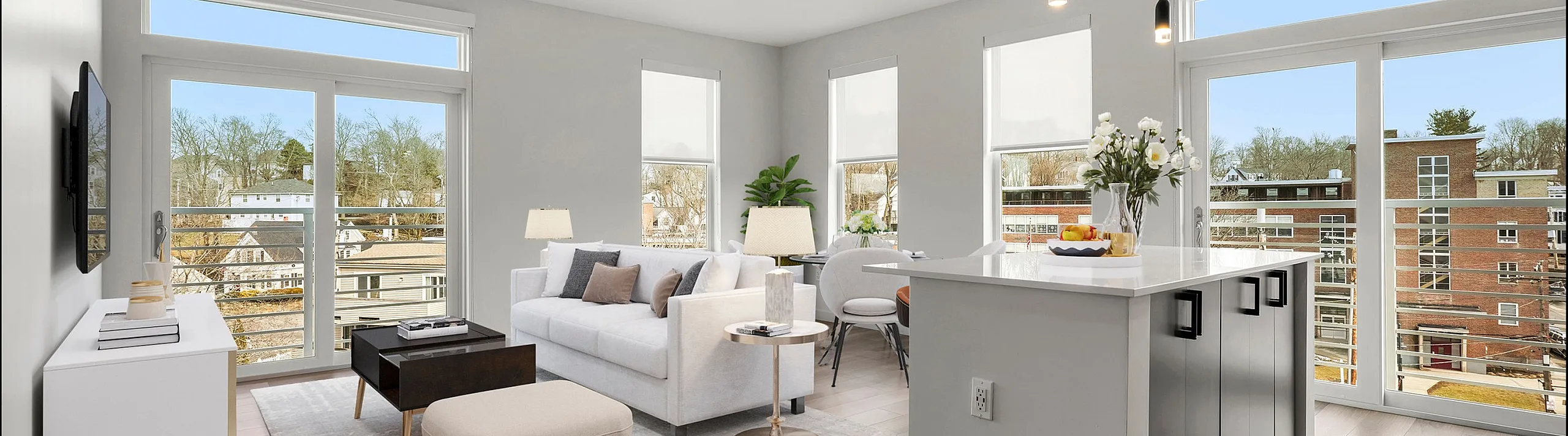 Bright and modern living area with sleek hardwood floors, cozy seating, and an open-concept kitchen featuring stylish pendant lighting. Large windows offer stunning views and ample natural light.
