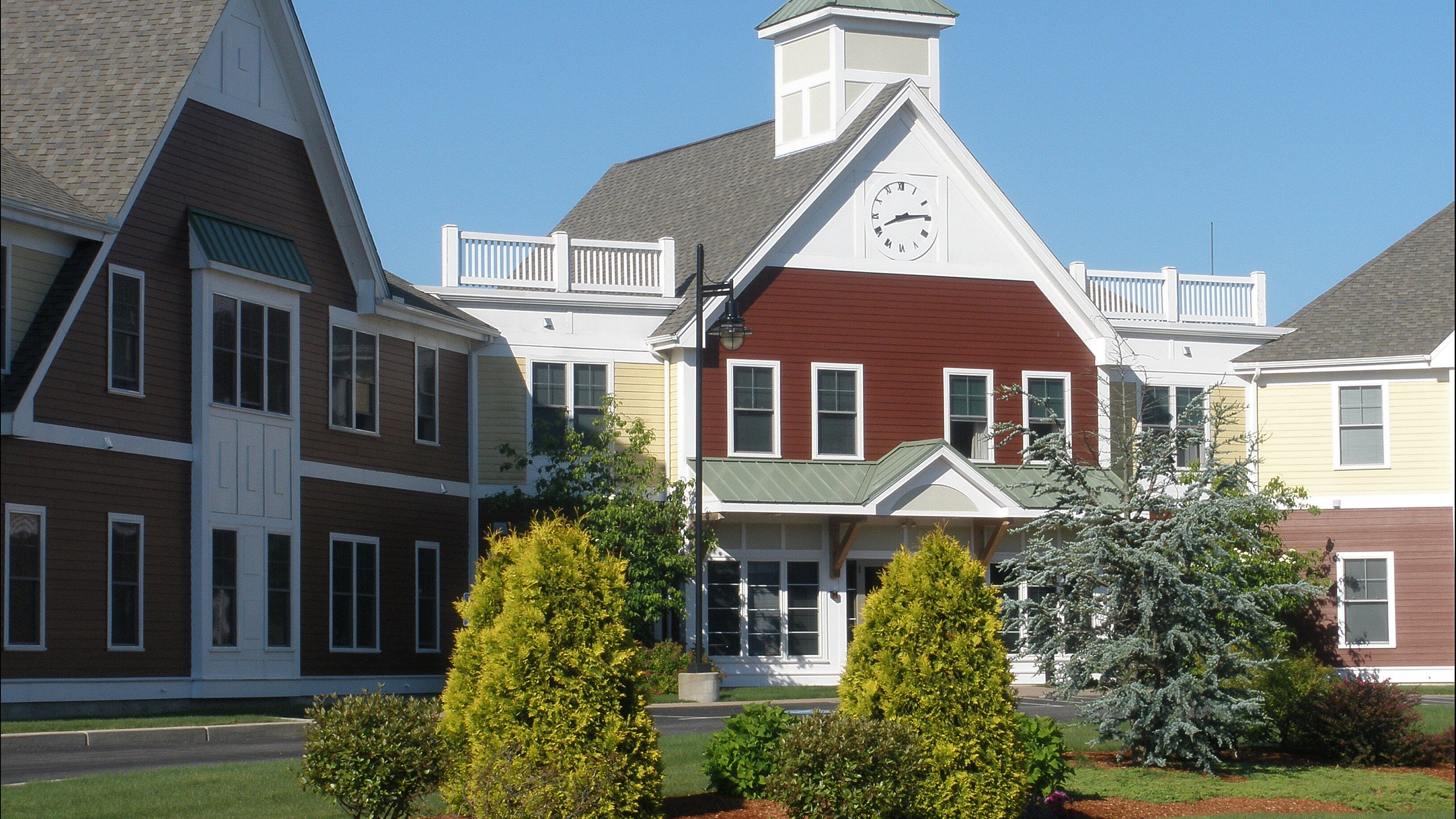 Charming residential building with a traditional design, featuring a striking clock tower and well-manicured landscape against a bright blue sky.