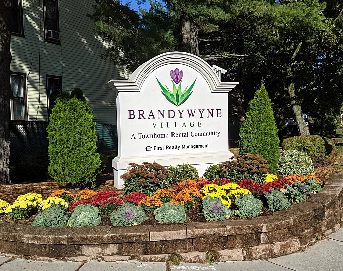 Charming entrance to Brandywyne Village, surrounded by colorful flowers and lush greenery, inviting you to a peaceful townhome community.