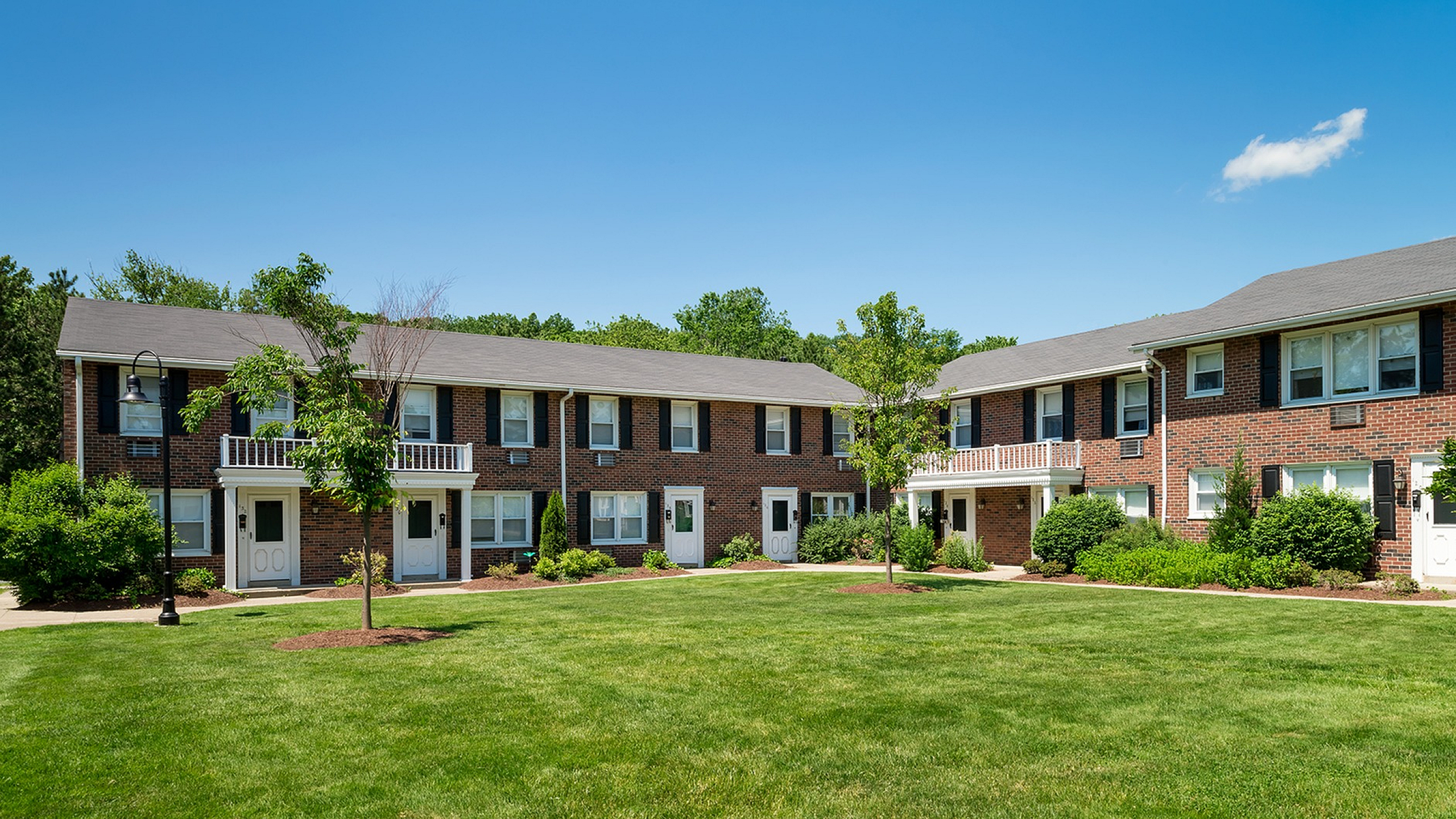 Charming brick apartment complex with lush green lawns and well-maintained landscaping, perfect for enjoying a sunny day.