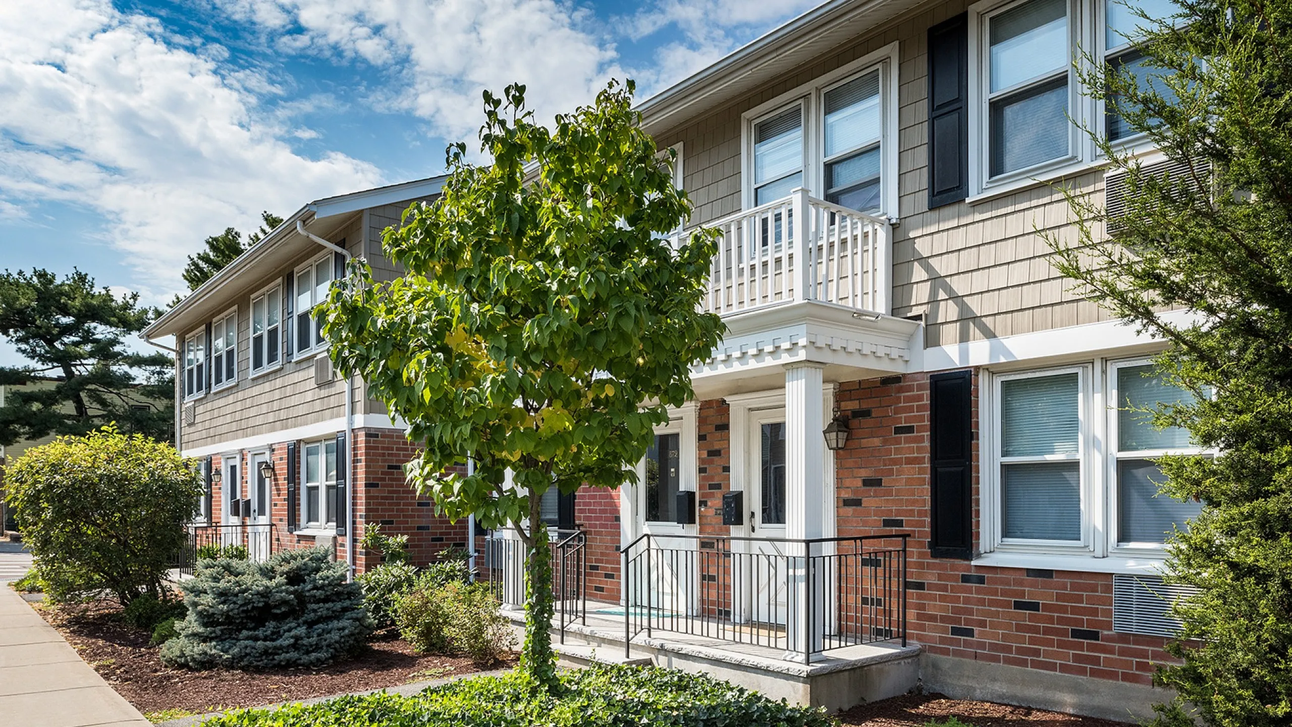 Charming apartment exterior with elegant brick facade, lush landscaping, and inviting entrance.