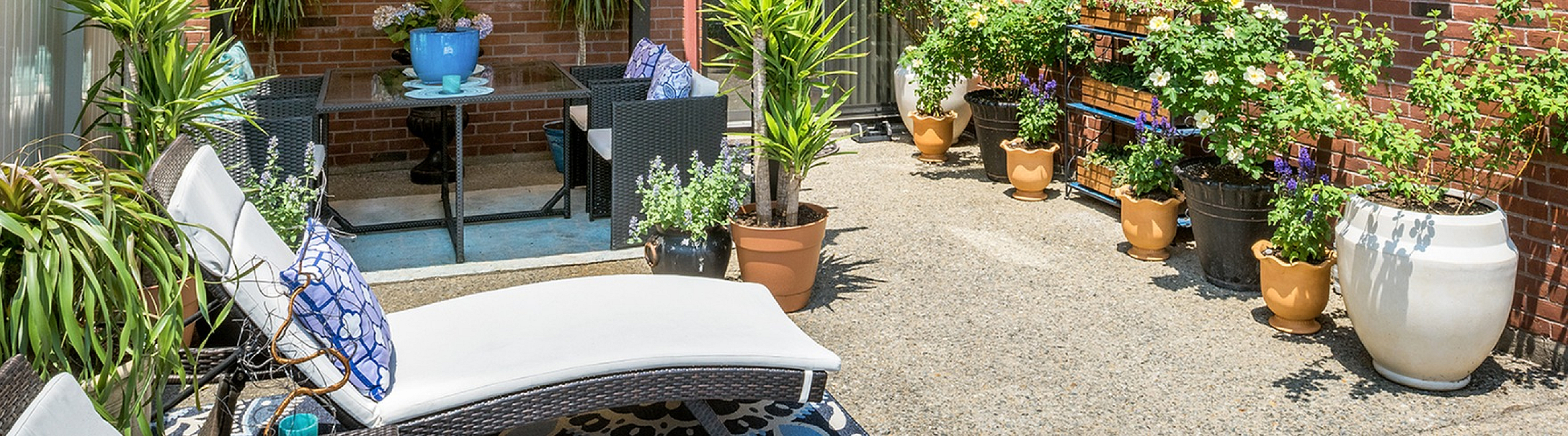 Charming outdoor patio with cozy seating, vibrant potted plants, and a stylish pergola against a brick wall backdrop.