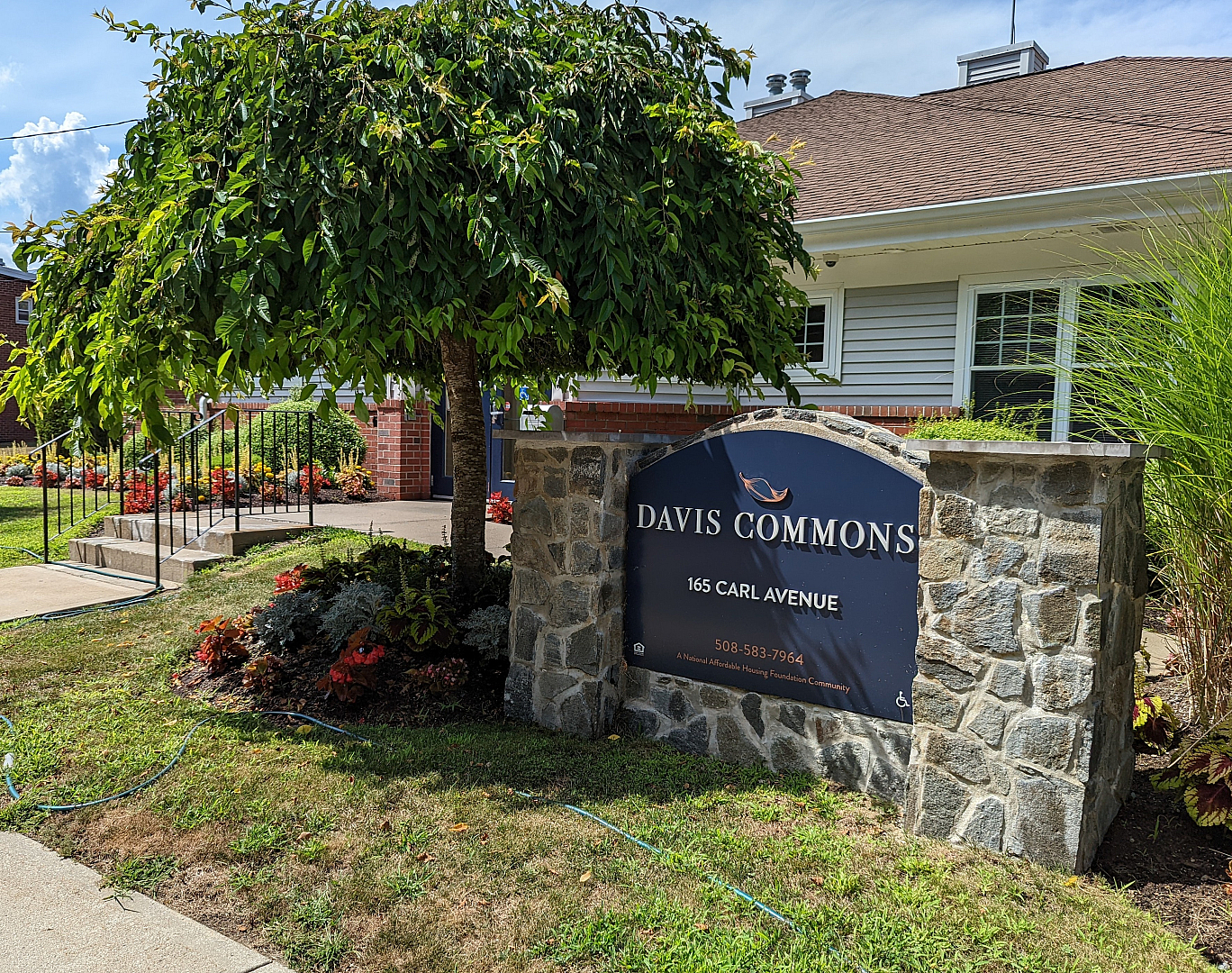 Welcoming entrance to Davis Commons, featuring a charming stone sign surrounded by lush landscaping and vibrant flowers.