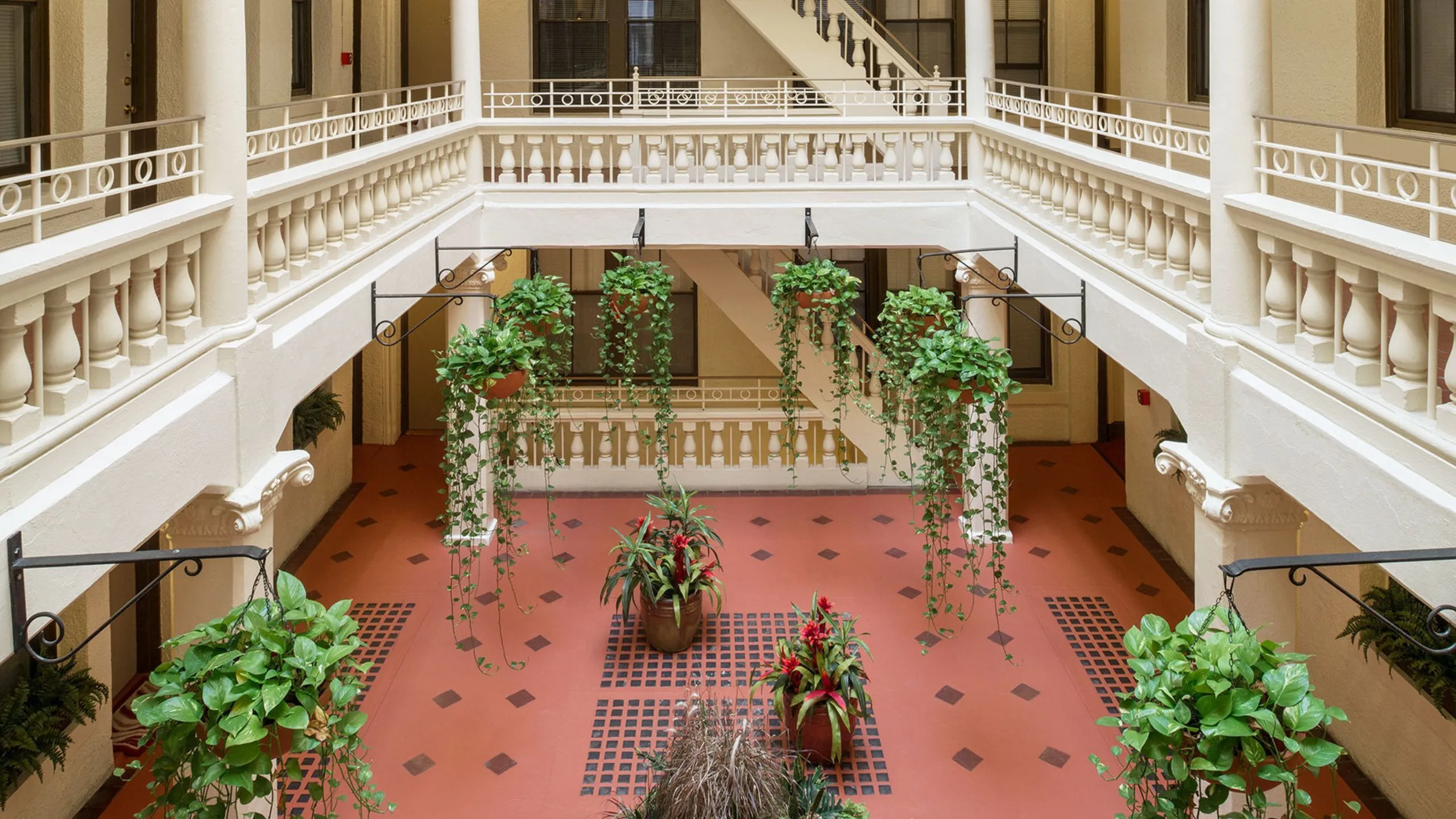 Elegant apartment atrium featuring classic white balustrades and lush hanging plants with vibrant red flowers.