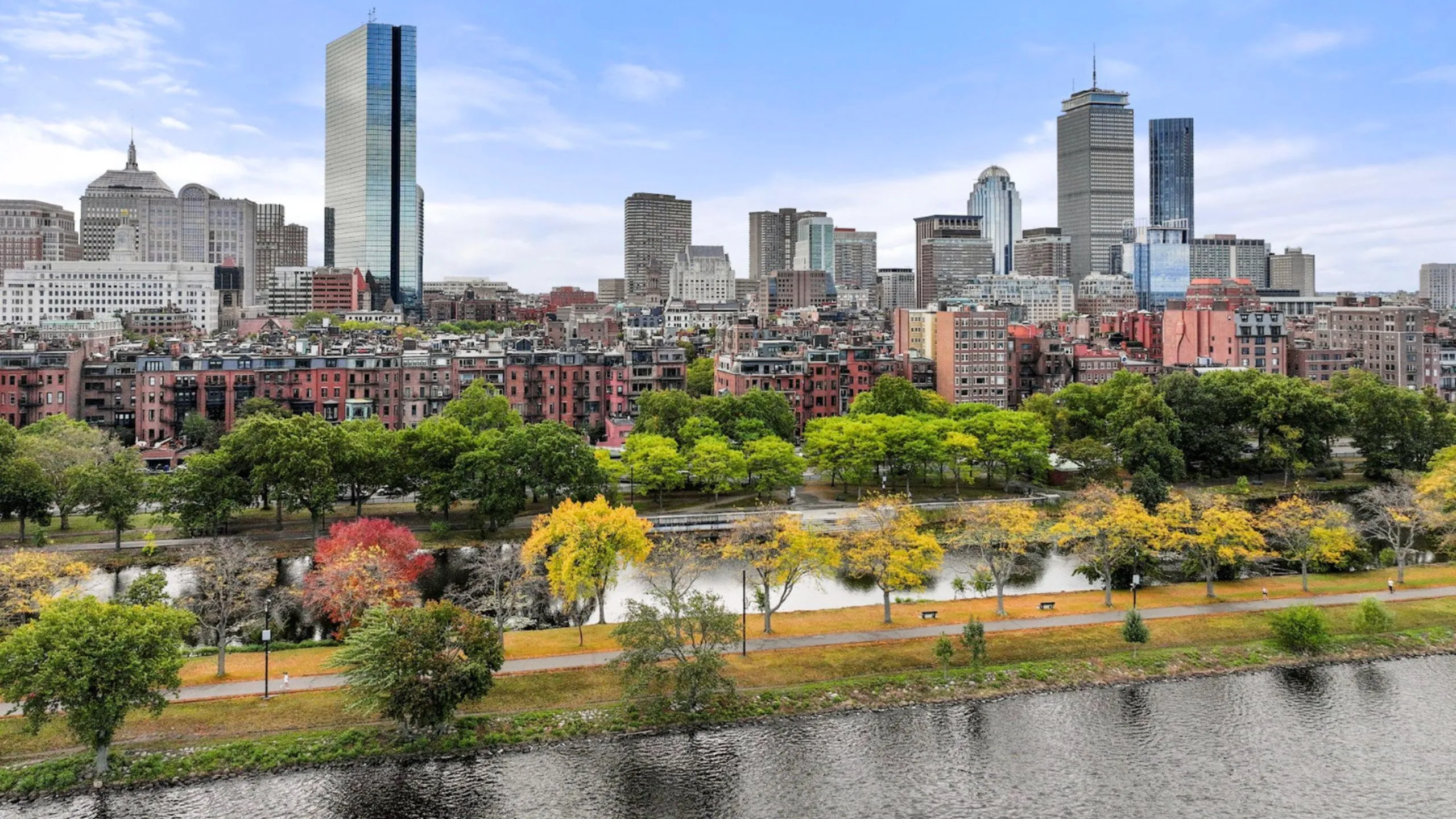 Breathtaking cityscape view featuring Boston's skyline with lush green parks and serene waterway in the foreground.