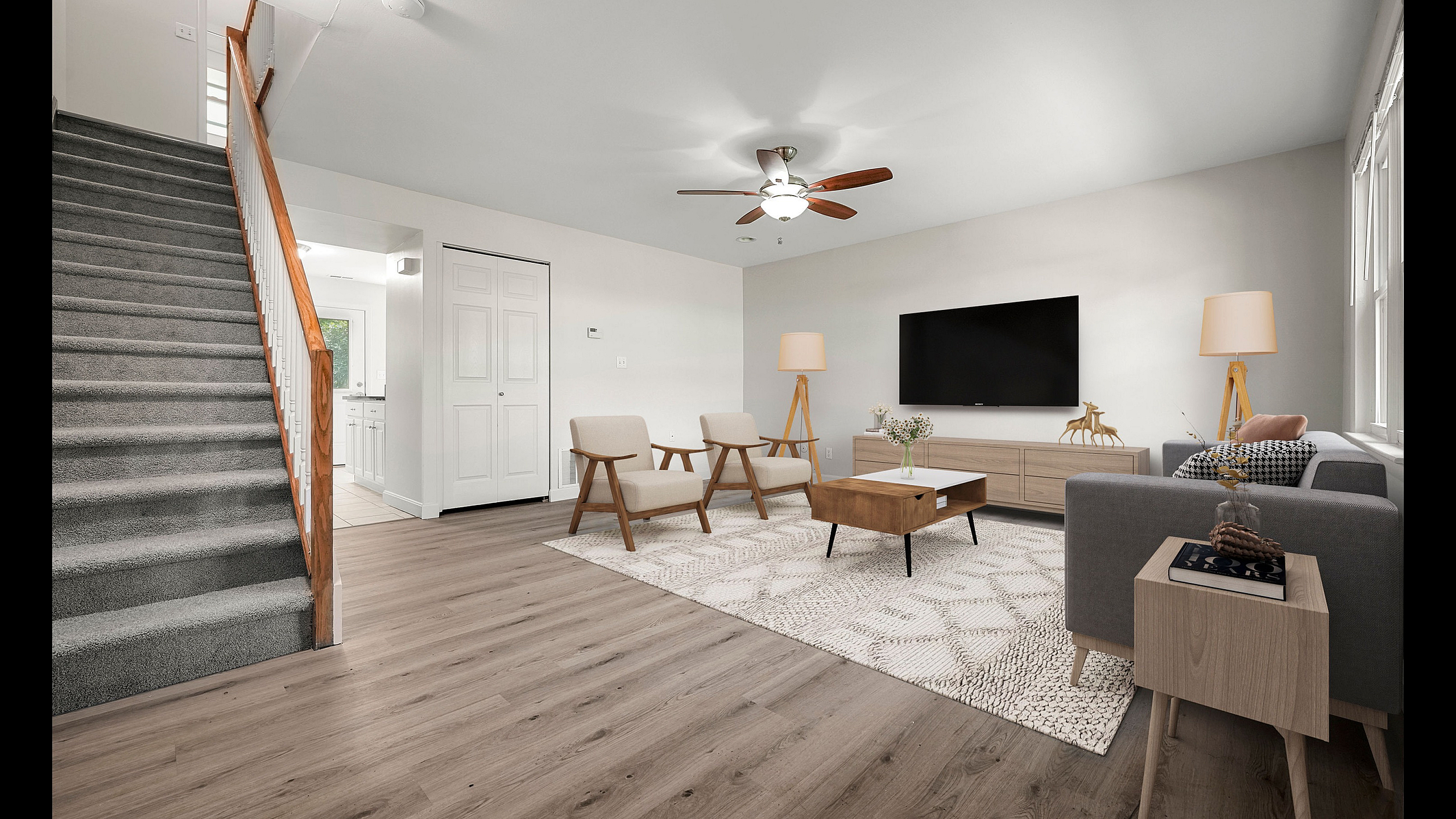 Modern living room with sleek hardwood floors, cozy seating, and stylish decor; open staircase leading to upper level.