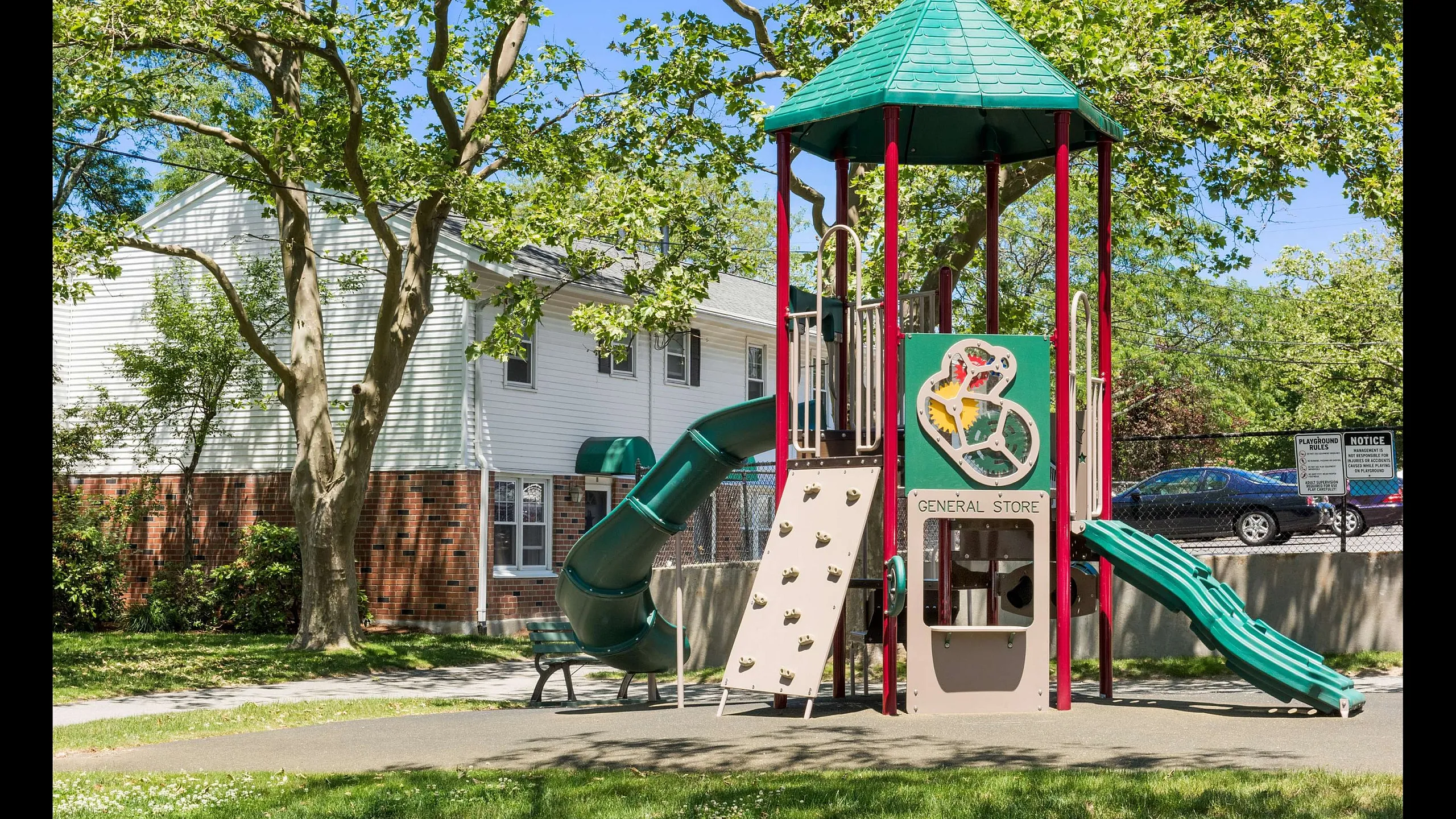 Charming apartment complex surrounded by lush greenery, featuring a vibrant playground with slides and climbing structures.