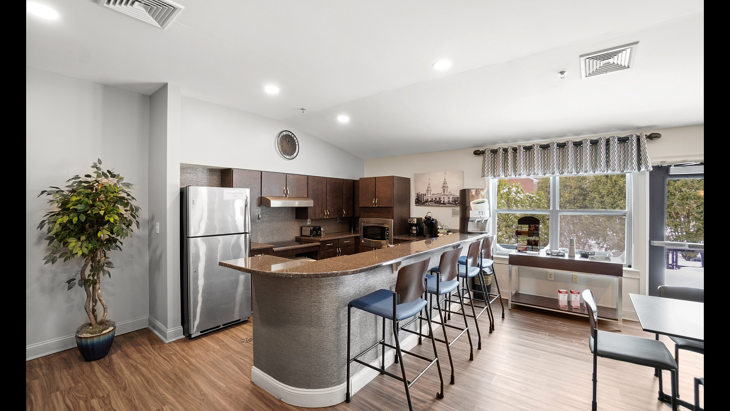 Modern kitchen featuring sleek countertops, elegant cabinetry, and a spacious breakfast bar with stylish seating, overlooking bright windows.