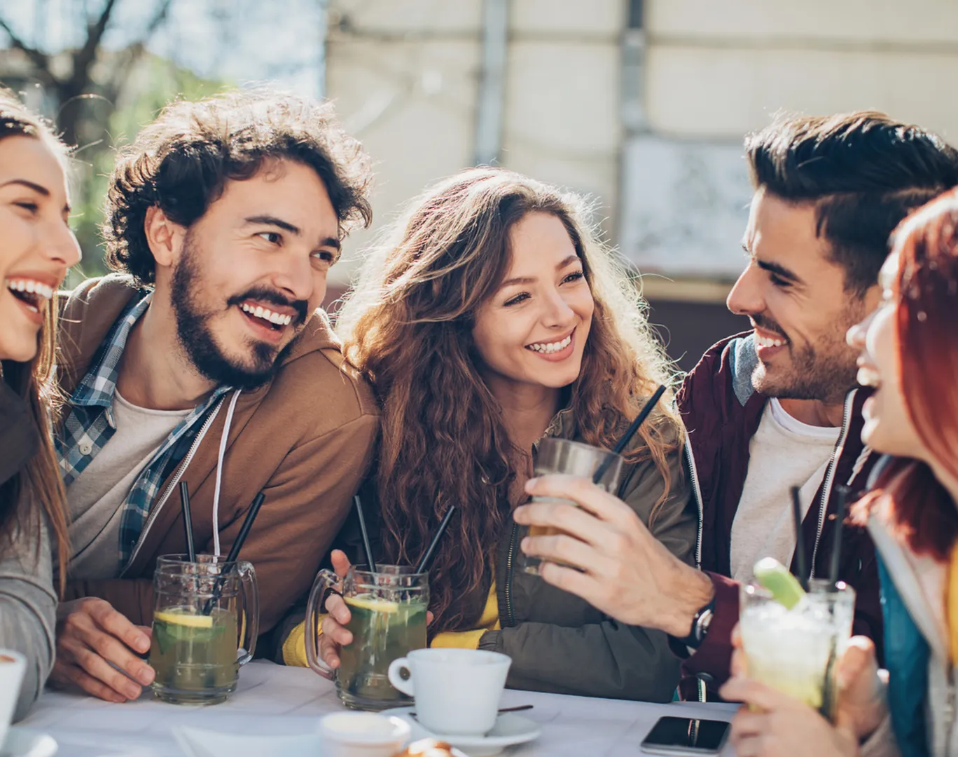 Group of friends enjoying drinks and laughter at an outdoor cafe.