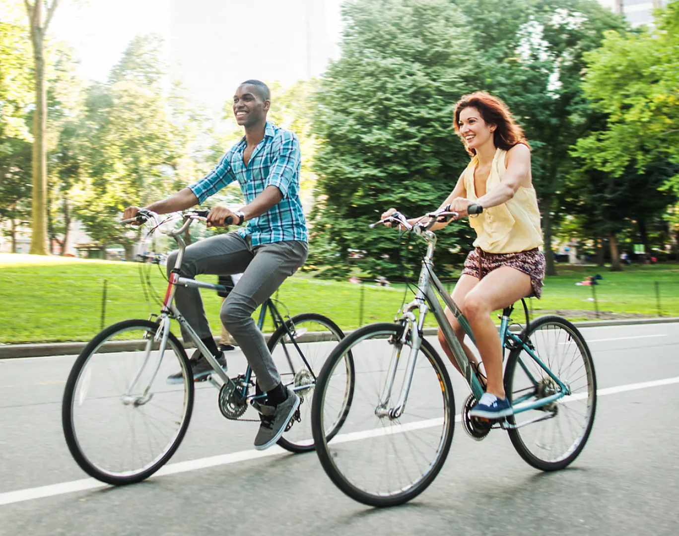 Joyful couple cycling together in a beautiful green urban park, enjoying a sunny and refreshing day outdoors.