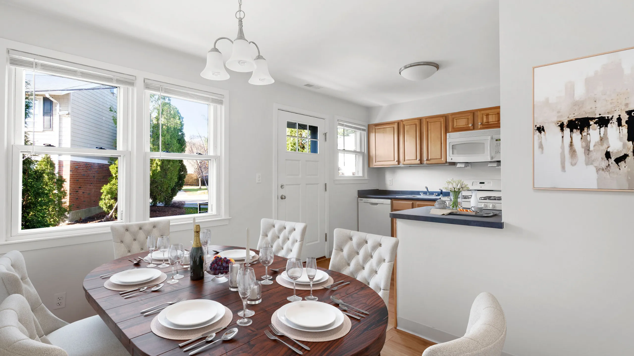 Bright and inviting dining area with elegant table setting, modern kitchen, and abundant natural light from large windows.