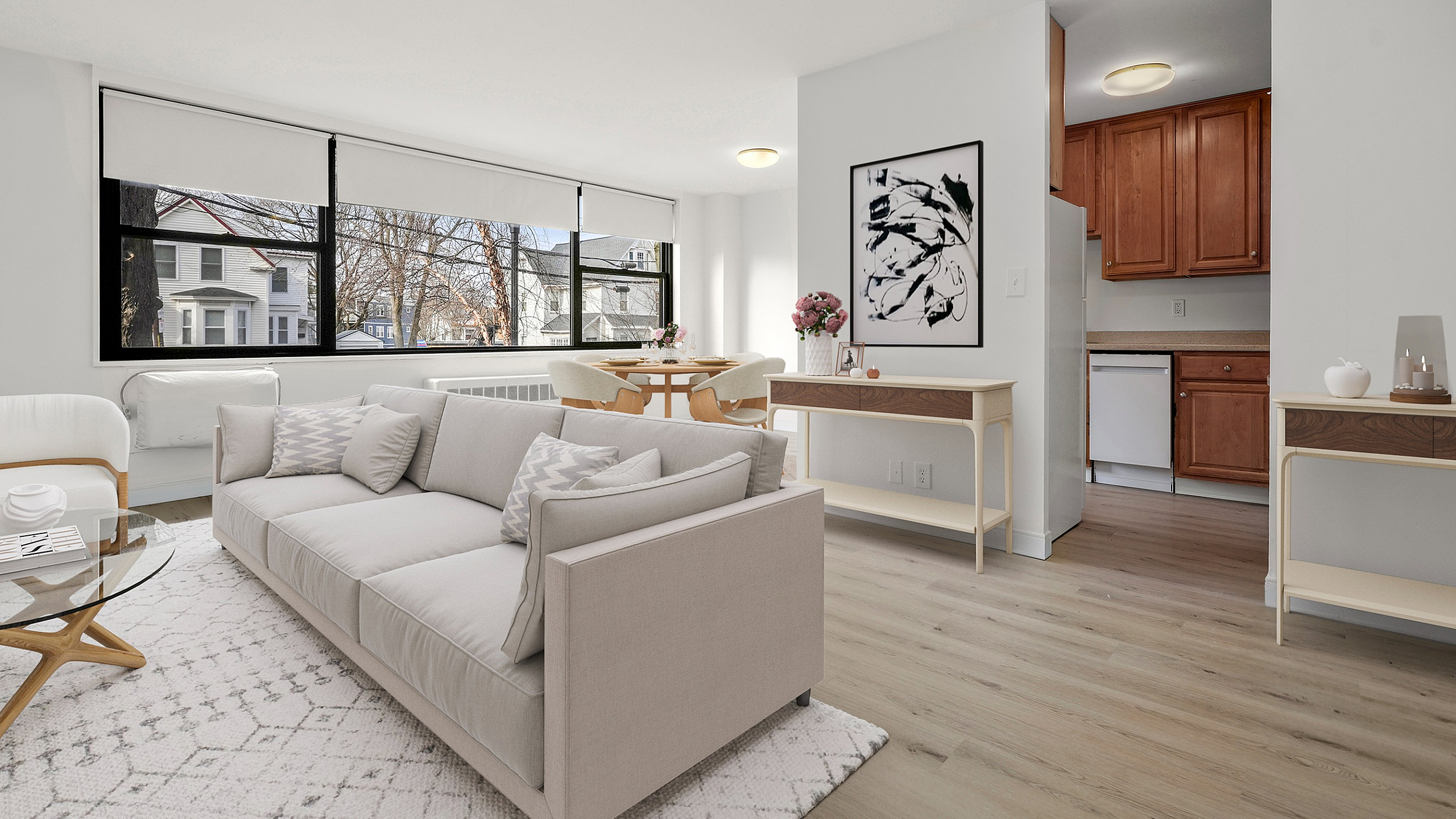Bright and airy open-concept living room with large windows, modern furnishings, and sleek hardwood floors, leading into a cozy kitchen area.