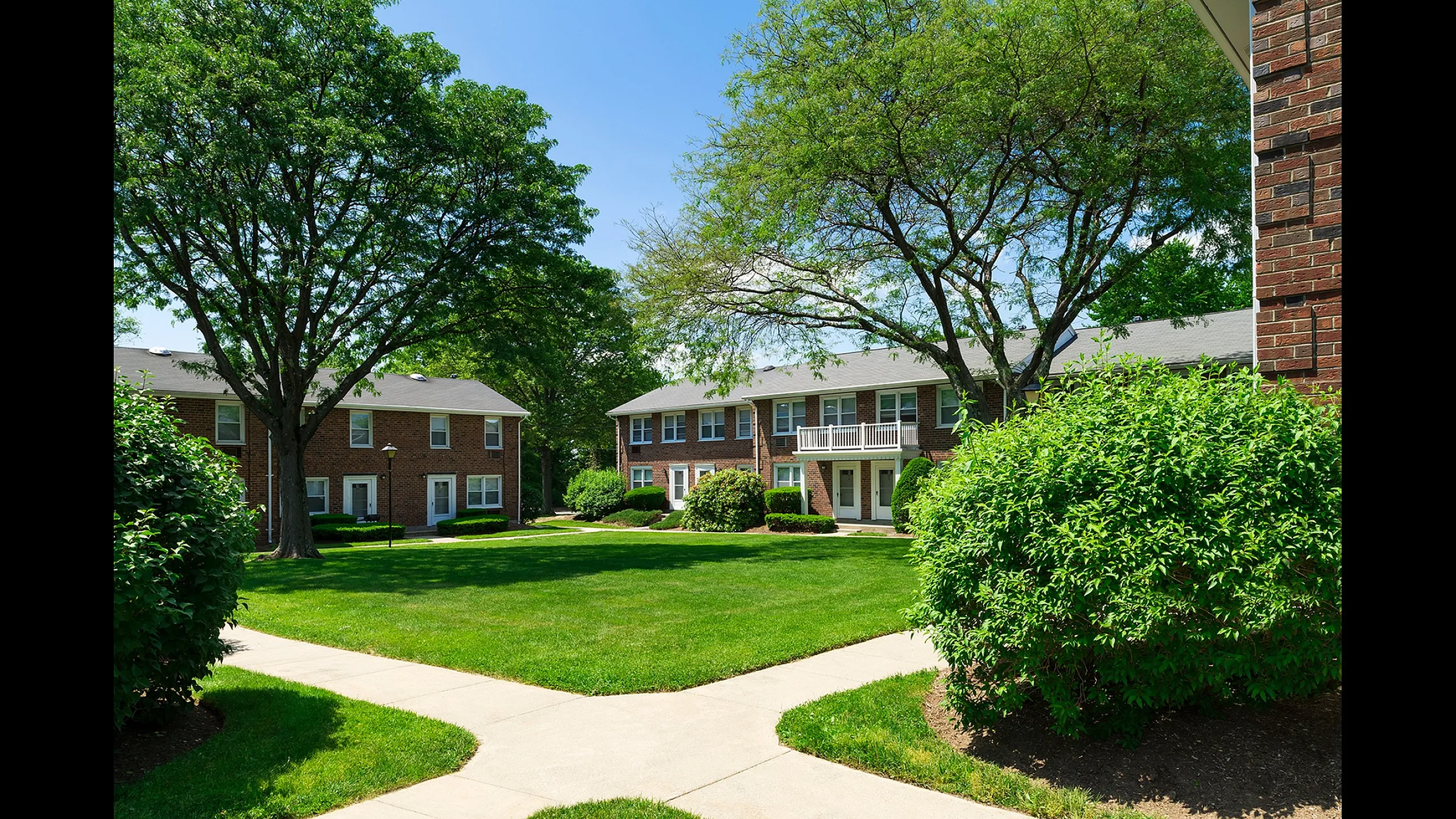 Charming apartment building surrounded by lush greenery and mature trees, offering a serene outdoor space and inviting pathways.