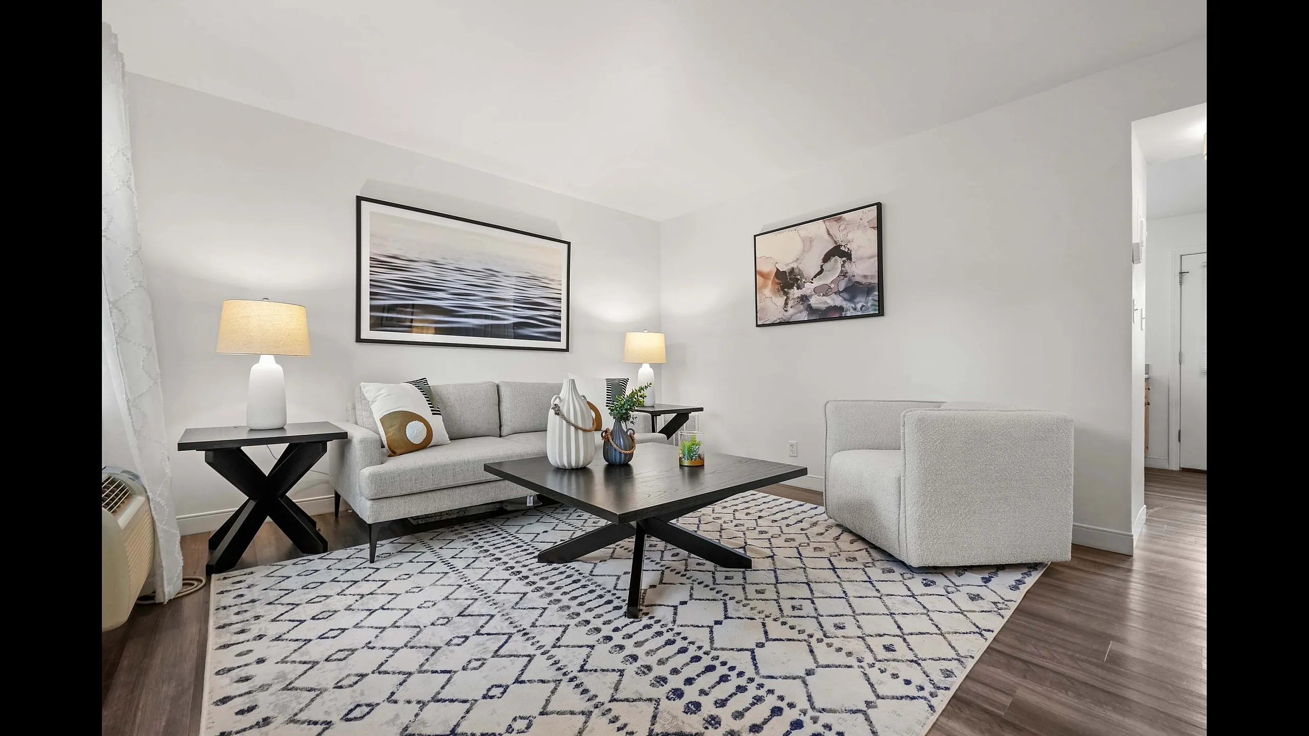 Elegant living room with modern decor, featuring a stylish gray sofa, chic armchair, and contemporary artwork. The room boasts a cozy ambiance with soft lighting and a plush patterned rug.