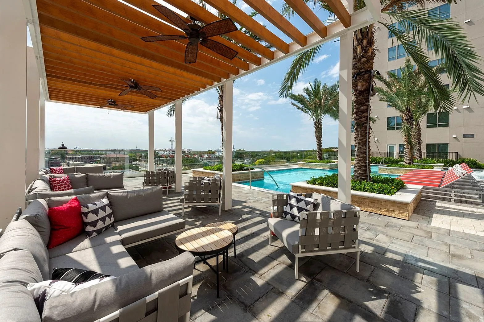 Luxurious outdoor lounge area featuring modern seating under a stylish pergola, overlooking a crystal-clear pool and surrounded by palm trees.