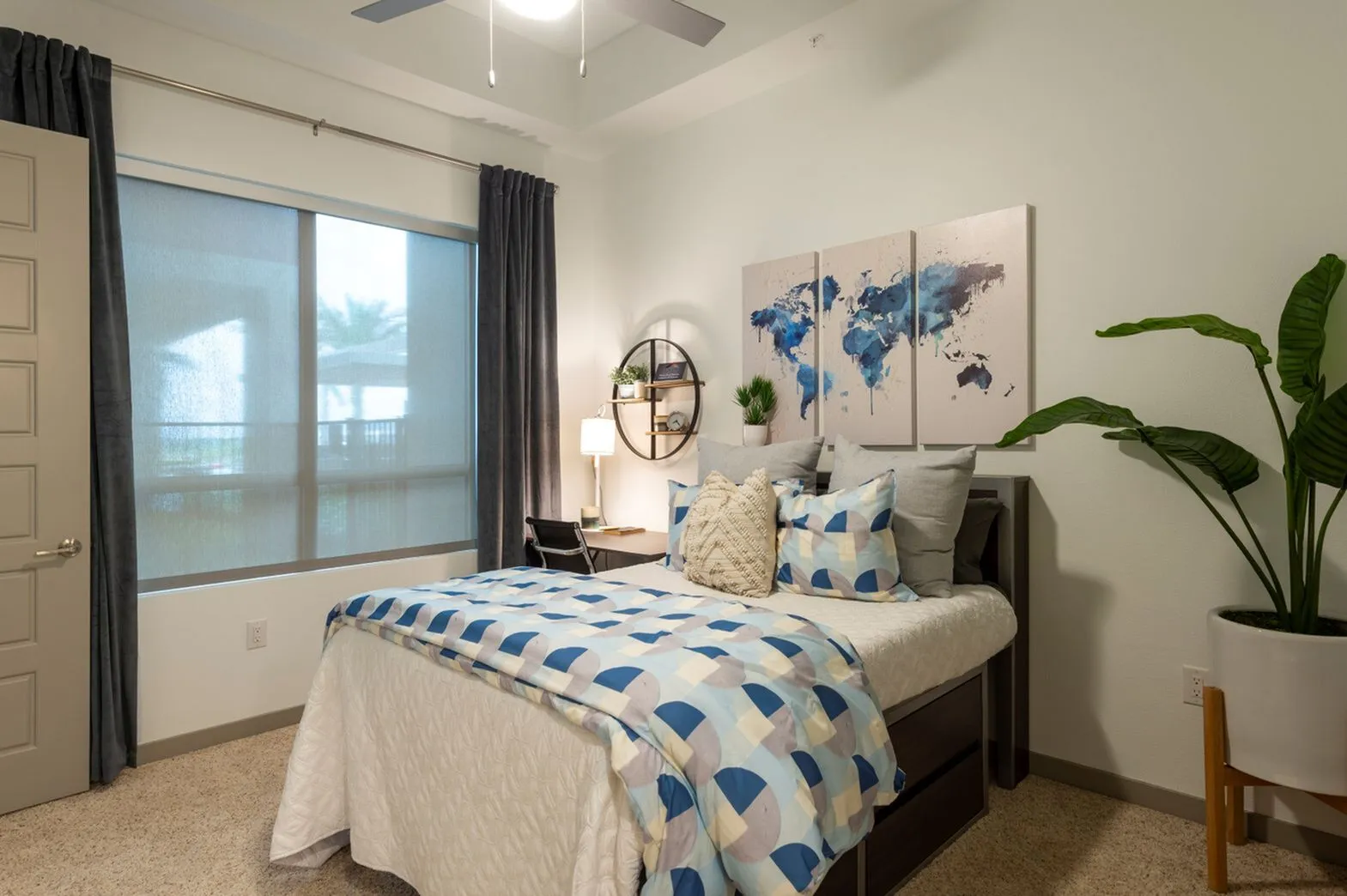 Inviting bedroom with stylish decor, featuring a cozy bed with blue and white bedding, modern world map artwork, and large window with elegant curtains.