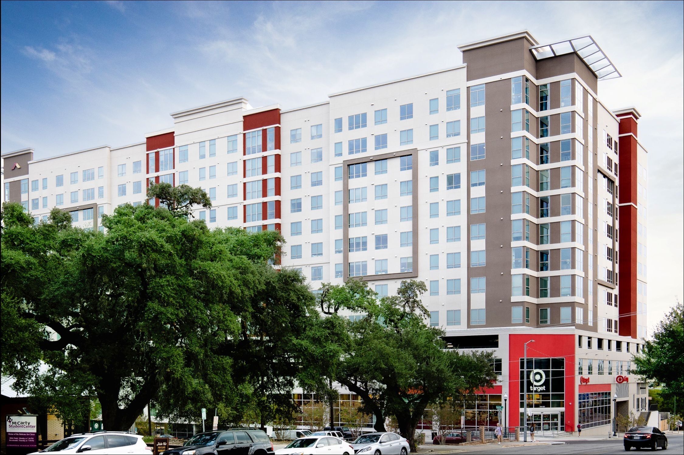 Modern high-rise building with sleek design, surrounded by lush greenery and featuring a convenient retail space at the base.