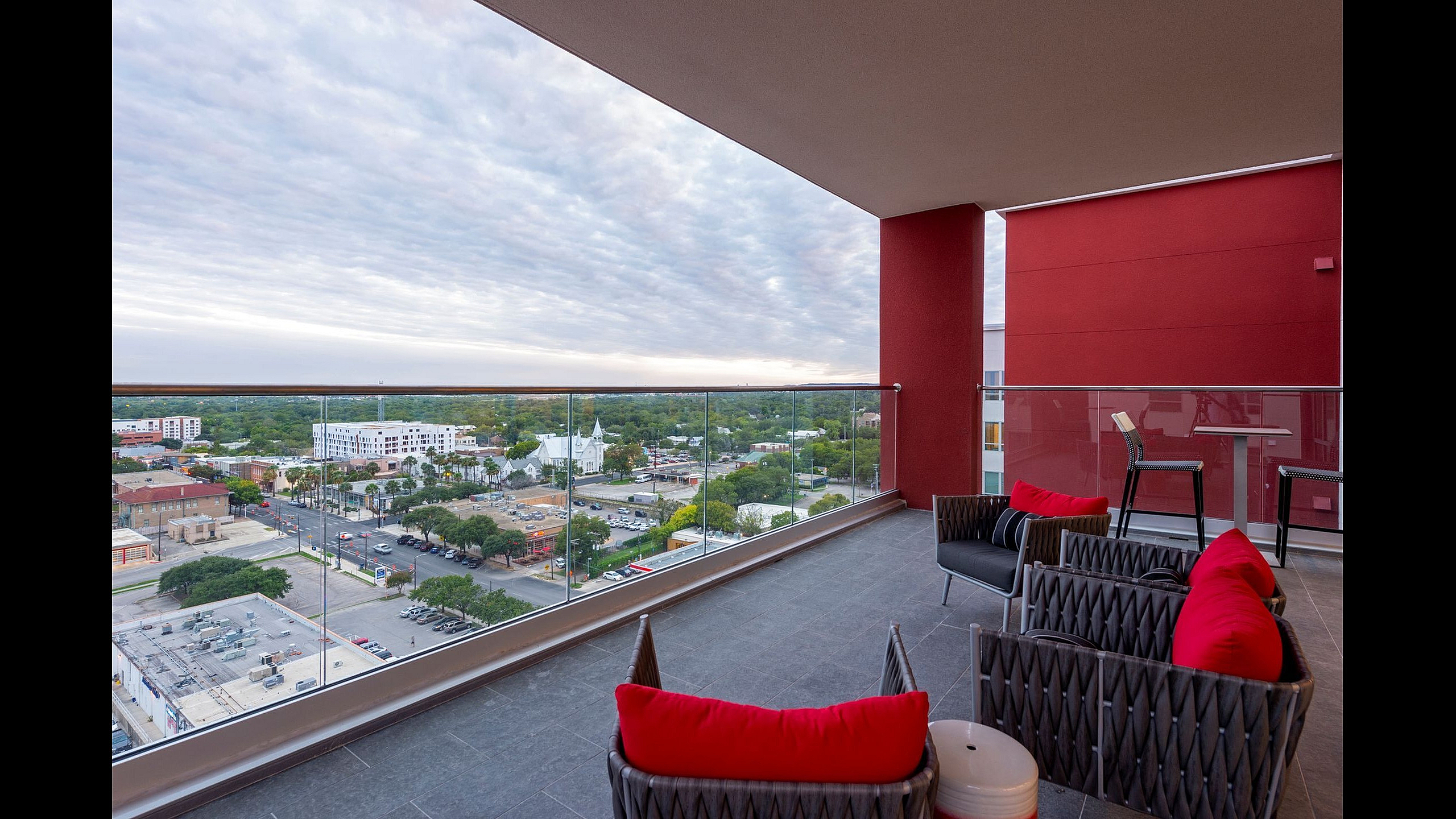 Luxurious urban balcony with stylish seating and panoramic city views, featuring elegant red accents and modern glass railing.