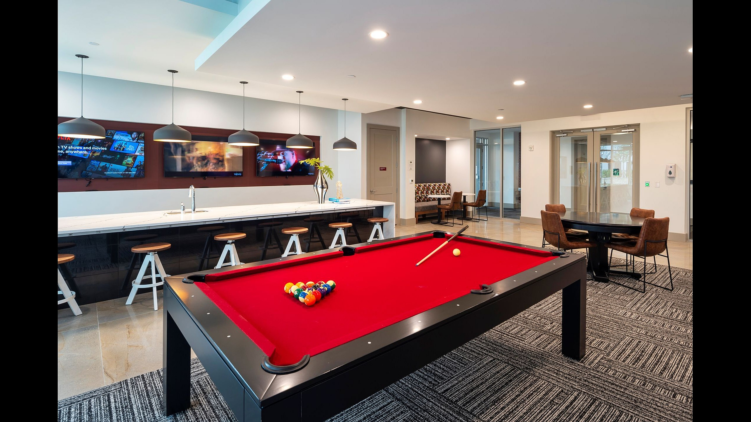 Modern apartment amenities featuring a vibrant red pool table, stylish bar seating, and cozy lounge area, perfect for entertainment.