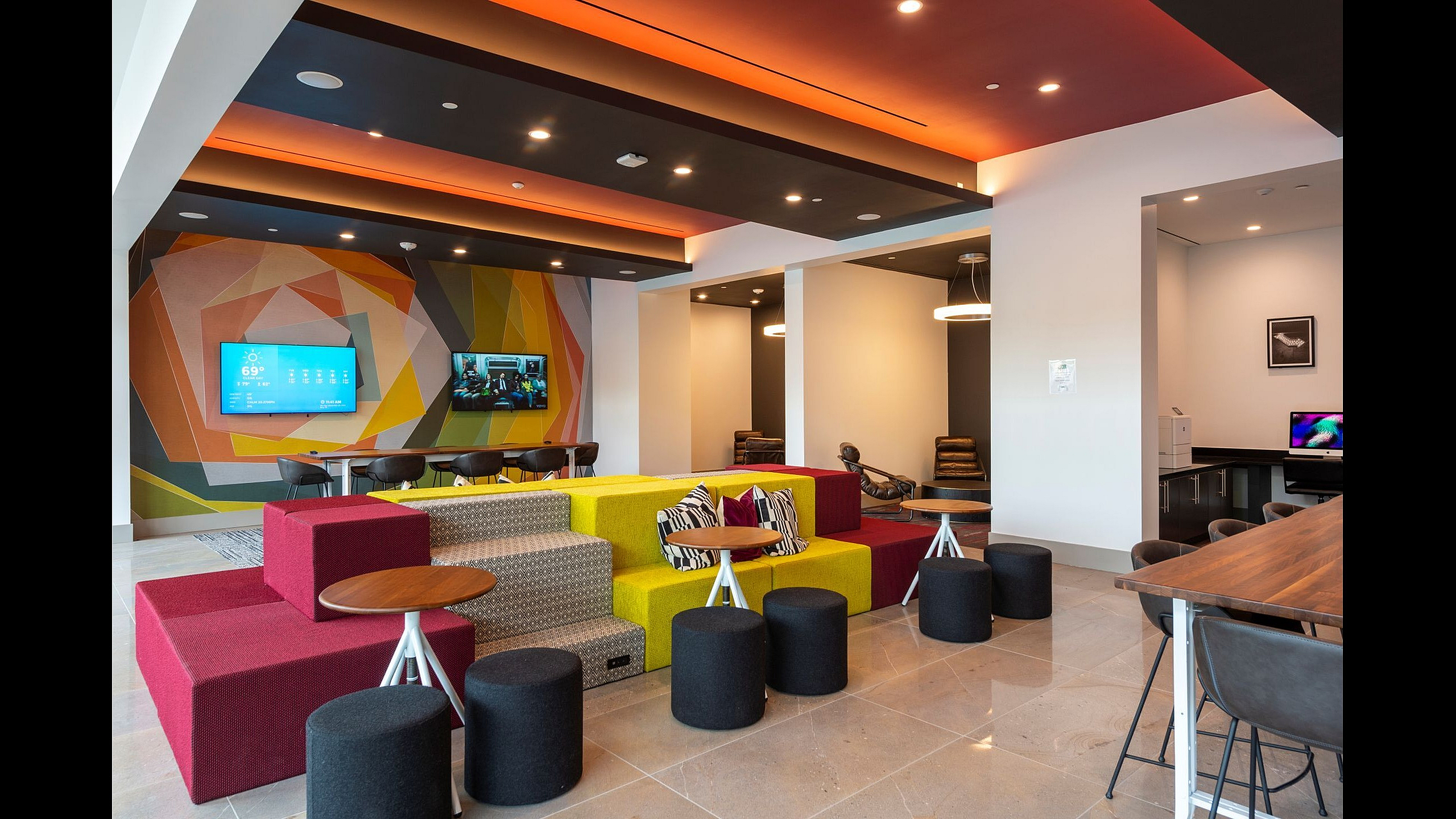 Vibrant and modern lounge area featuring colorful seating, stylish tables, and a dynamic wall design with integrated flat-screen TVs.