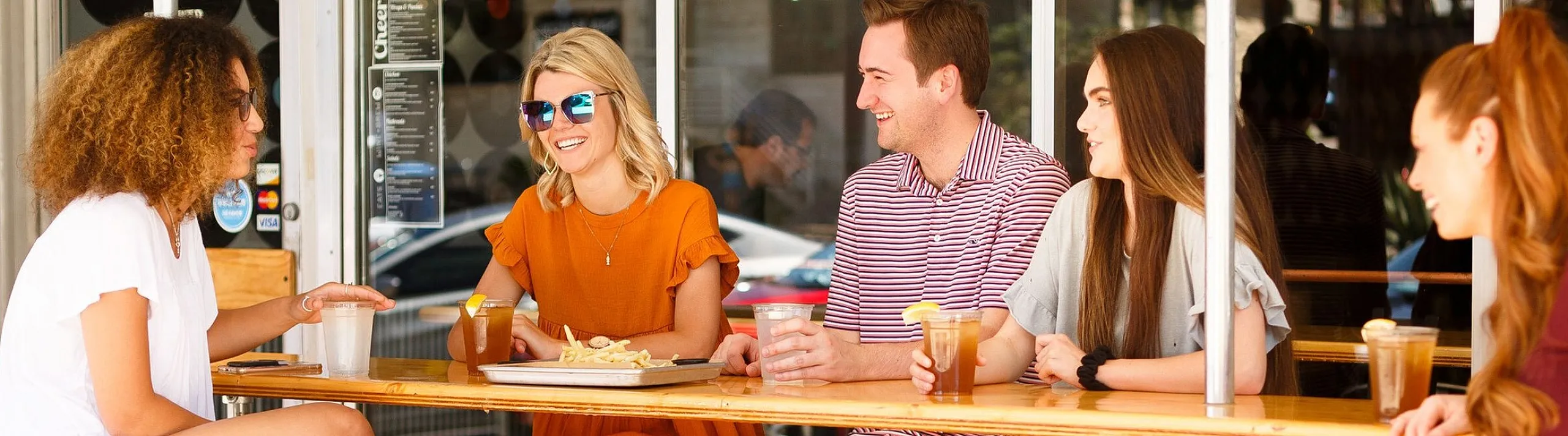 Vibrant group of friends enjoying drinks and socializing at an outdoor cafe on a sunny day.