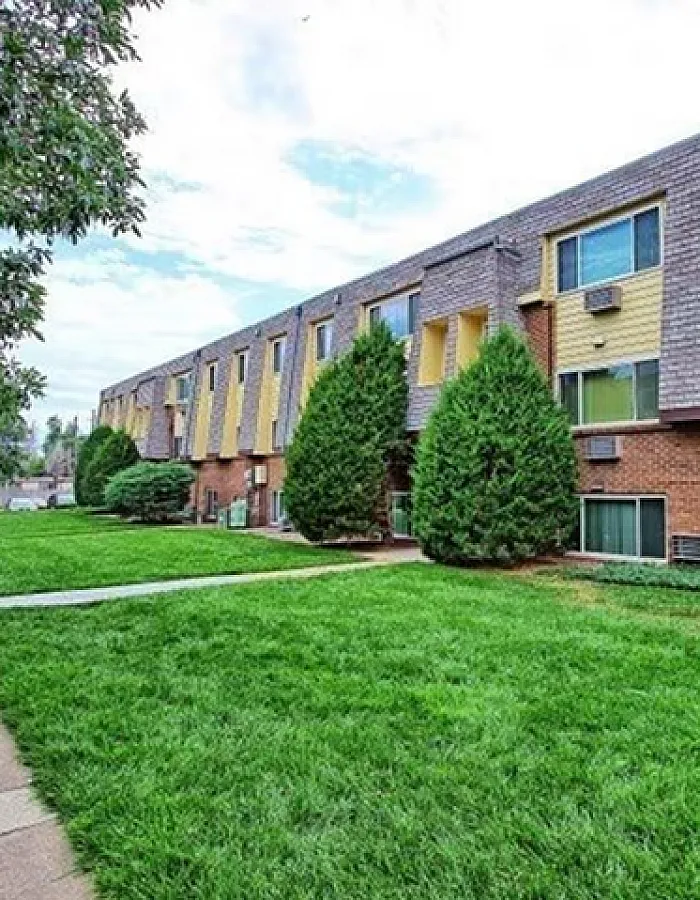 Charming brick apartment complex with lush green lawns and vibrant yellow accents, offering a serene living environment.