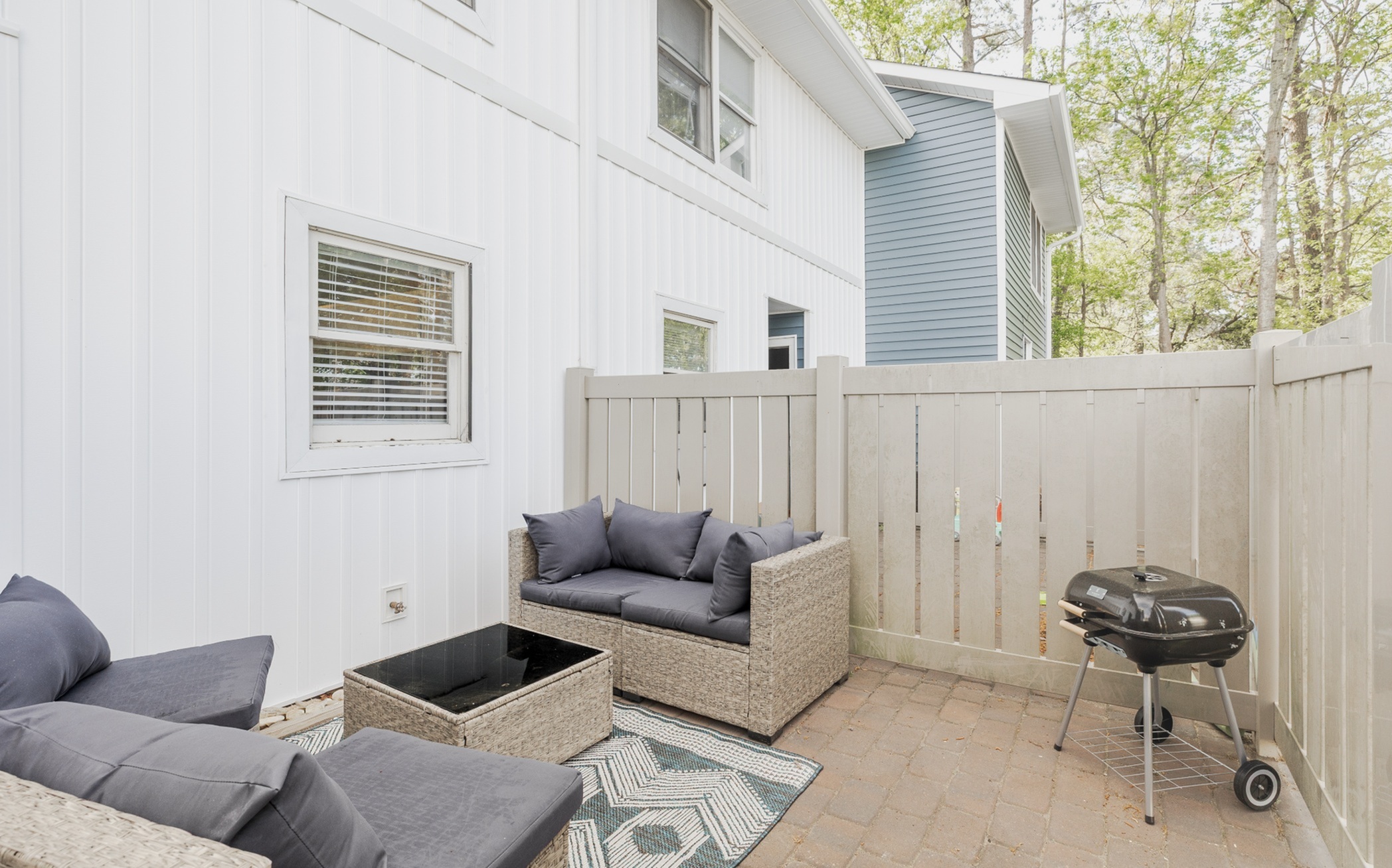 Charming outdoor patio with cozy wicker seating, stylish cushions, and a barbecue grill, perfect for relaxing and entertaining.