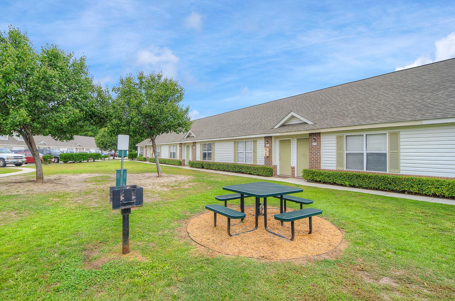 Charming apartment community with lush greenery, picnic area, and convenient parking.