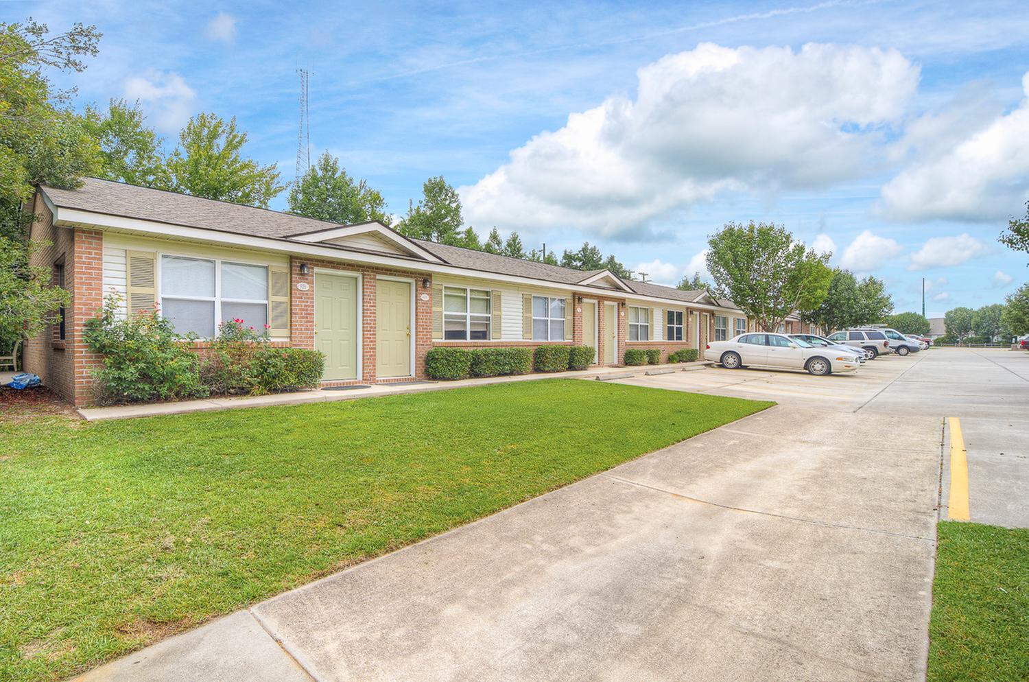 Charming apartment complex with inviting entrances, lush landscaping, and ample parking under a picturesque sky.