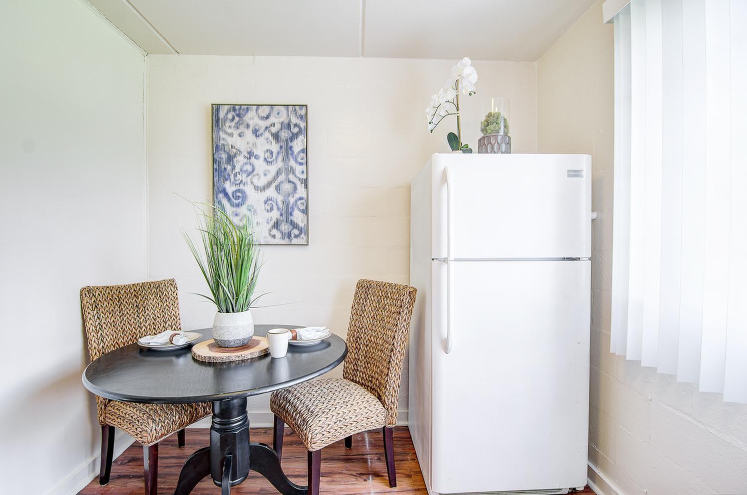 Charming dining nook with a modern round table, wicker chairs, and vibrant decor beside a sleek white refrigerator.