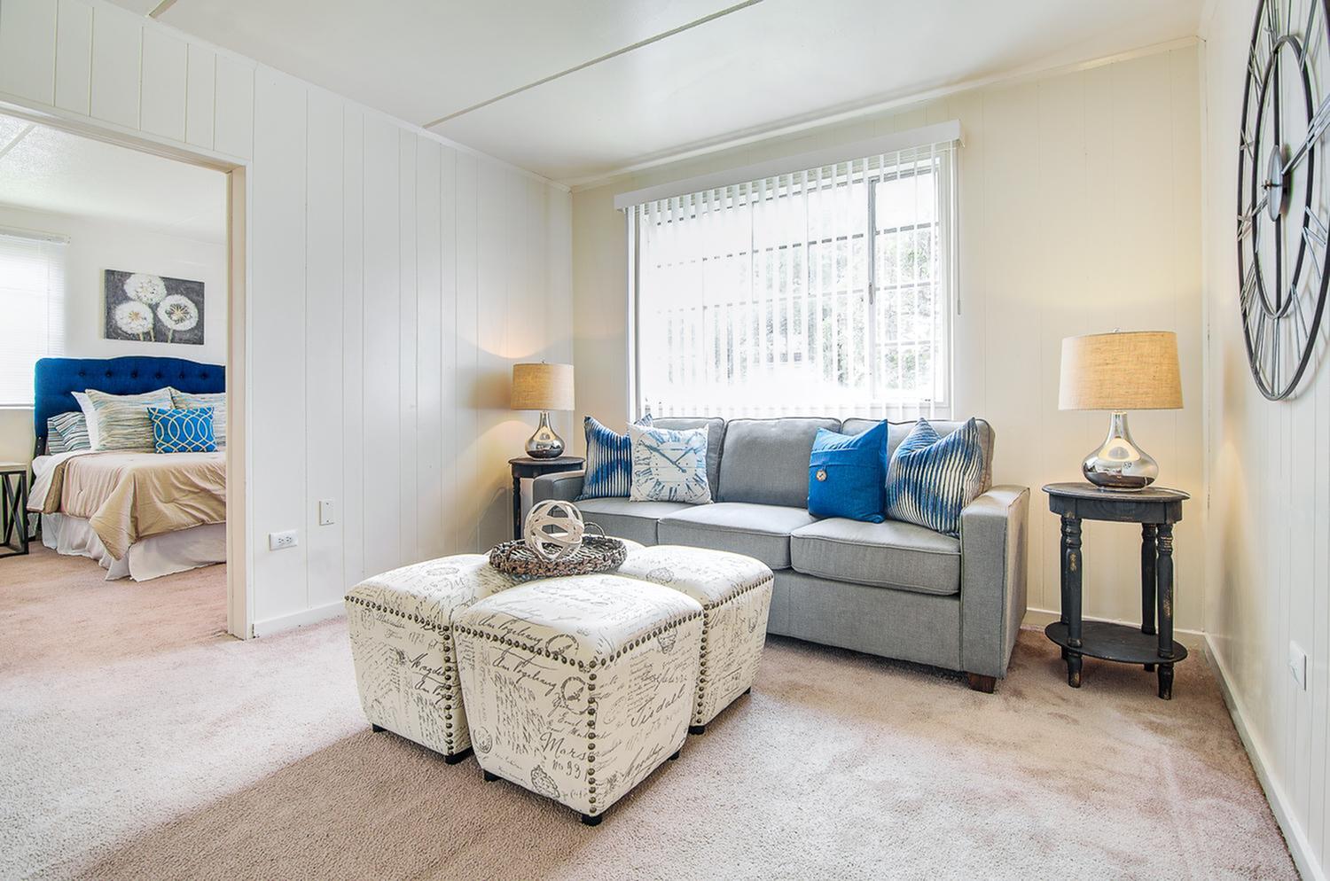 Inviting living room with plush gray sofa, vibrant blue cushions, and elegant decor, leading to a cozy bedroom with a striking blue headboard.