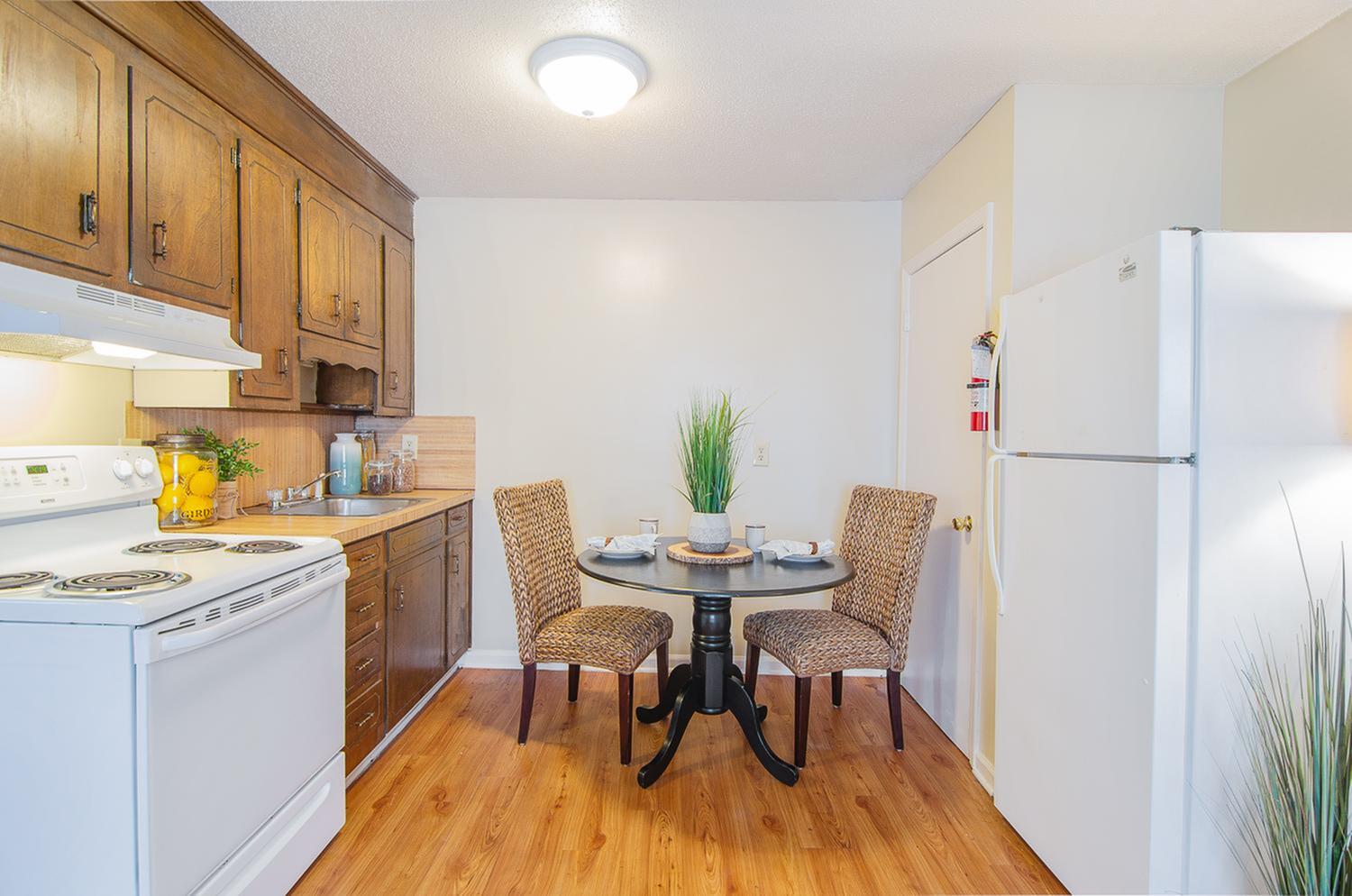 Charming kitchen with vintage wooden cabinets, bright laminate flooring, and a cozy dining nook featuring a round table and stylish wicker chairs.