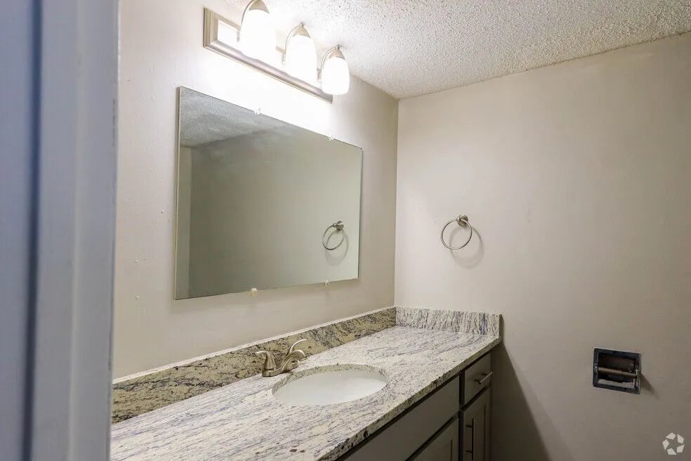 Elegant bathroom featuring a sleek granite countertop with a built-in sink, large mirror, and contemporary lighting.