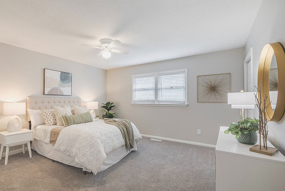 Bright and inviting bedroom featuring elegant decor, plush bedding, and soft carpet flooring, with natural light streaming through large windows.