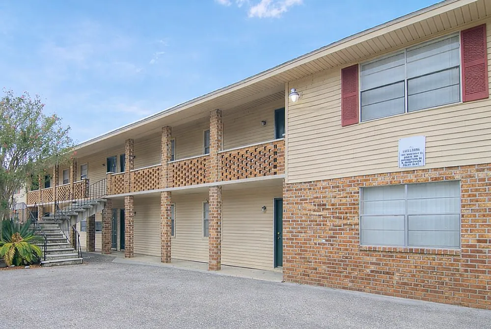 Charming apartment building with brick facade, cozy exterior staircases, and lush greenery, perfect for sunny living.