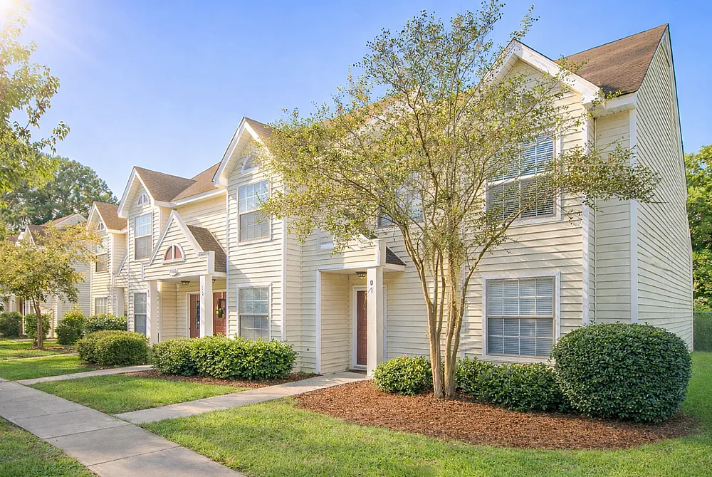 Charming townhouses with classic architecture, featuring white siding and welcoming front porches, surrounded by lush greenery.