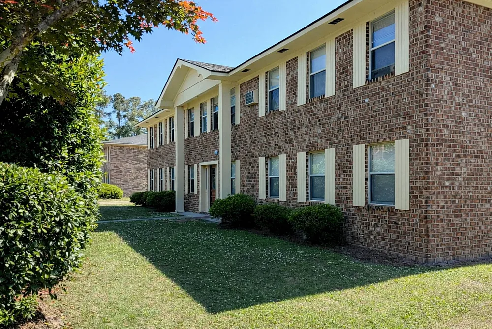 Charming brick apartment building with classic exterior, surrounded by lush greenery and vibrant landscape.
