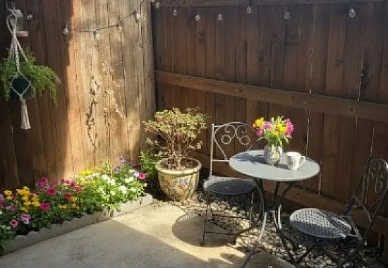 Charming patio oasis with cozy bistro set, vibrant flowers, and wooden privacy fence, perfect for relaxing.