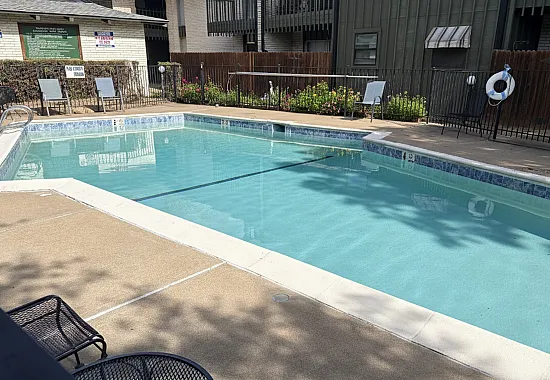 Inviting outdoor swimming pool with pristine water, surrounded by lush greenery and comfortable lounge chairs, offering a perfect relaxation spot in the apartment complex.