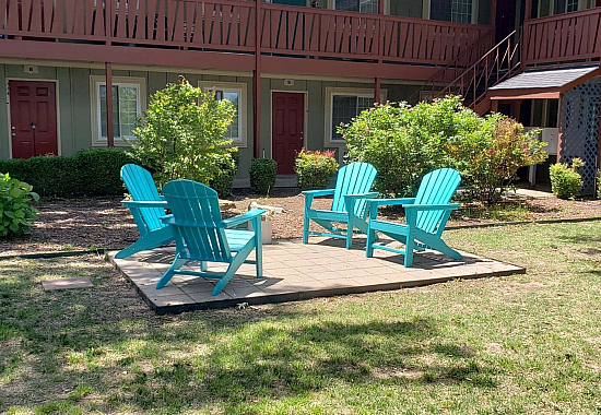Charming outdoor seating area with vibrant turquoise chairs surrounded by lush greenery, offering a welcoming ambiance in a cozy apartment courtyard.